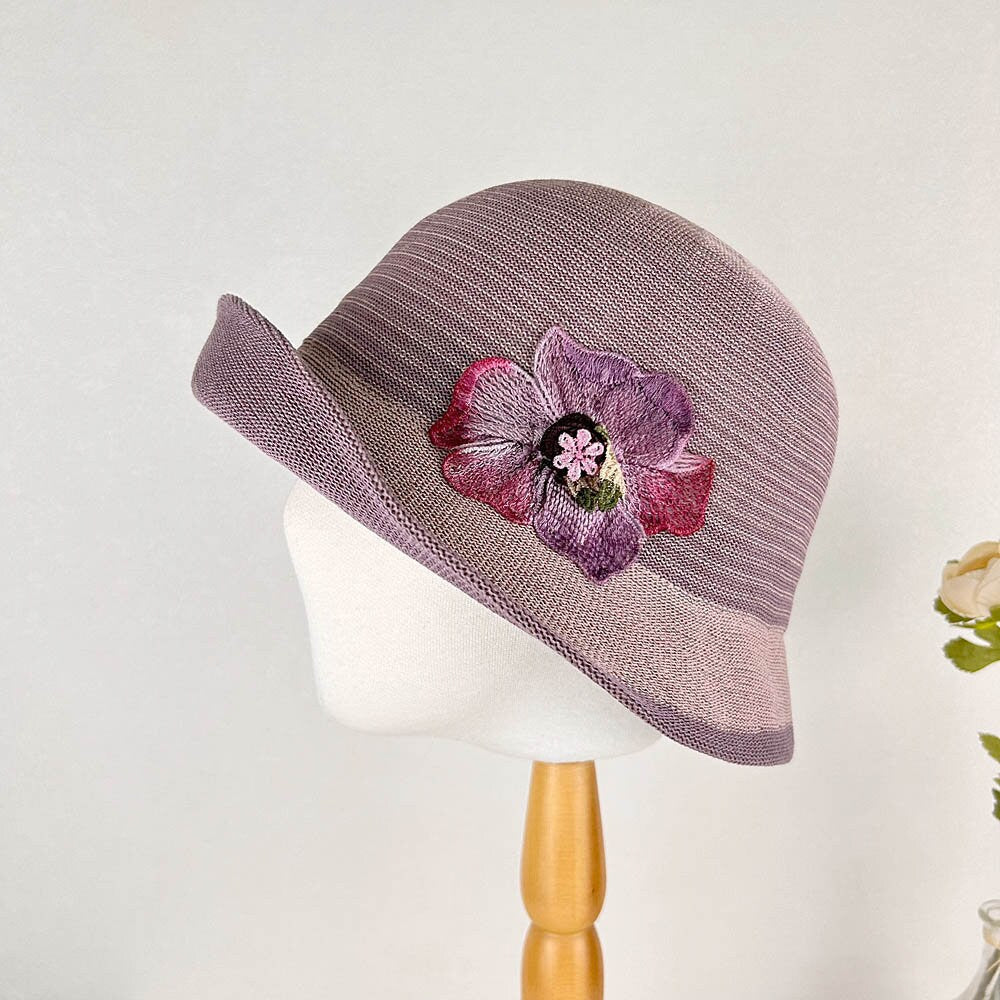 Purple cloche hat with a wide brim and a large, intricately embroidered floral crown detail.