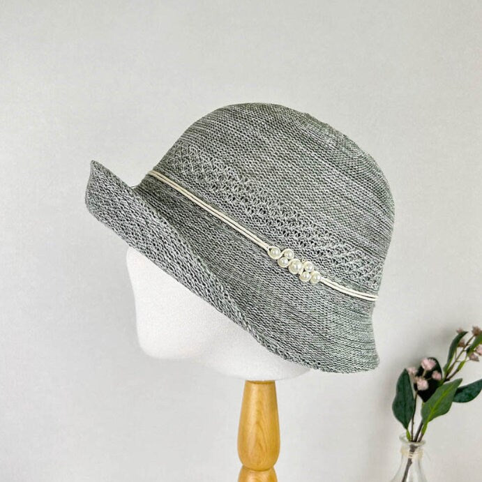 Gray woven alexandra hat with a white band and pearl accents. Perfect for sun protection and style.
