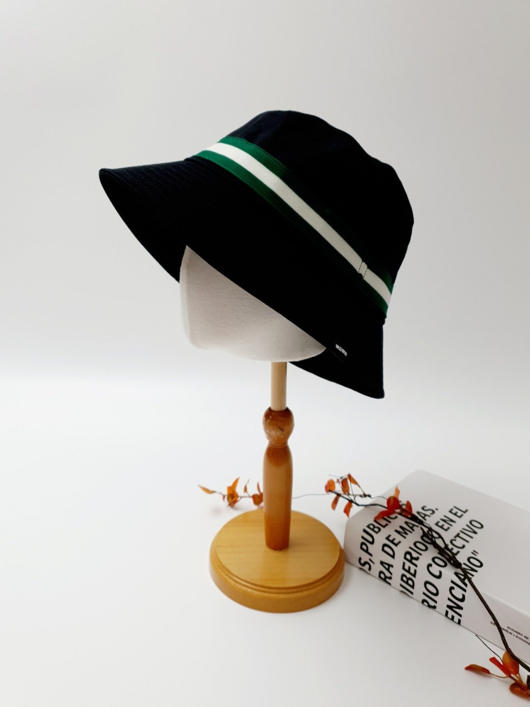 DAYTONA black bucket hat with a sporty green and white stripe, displayed on a wooden stand.