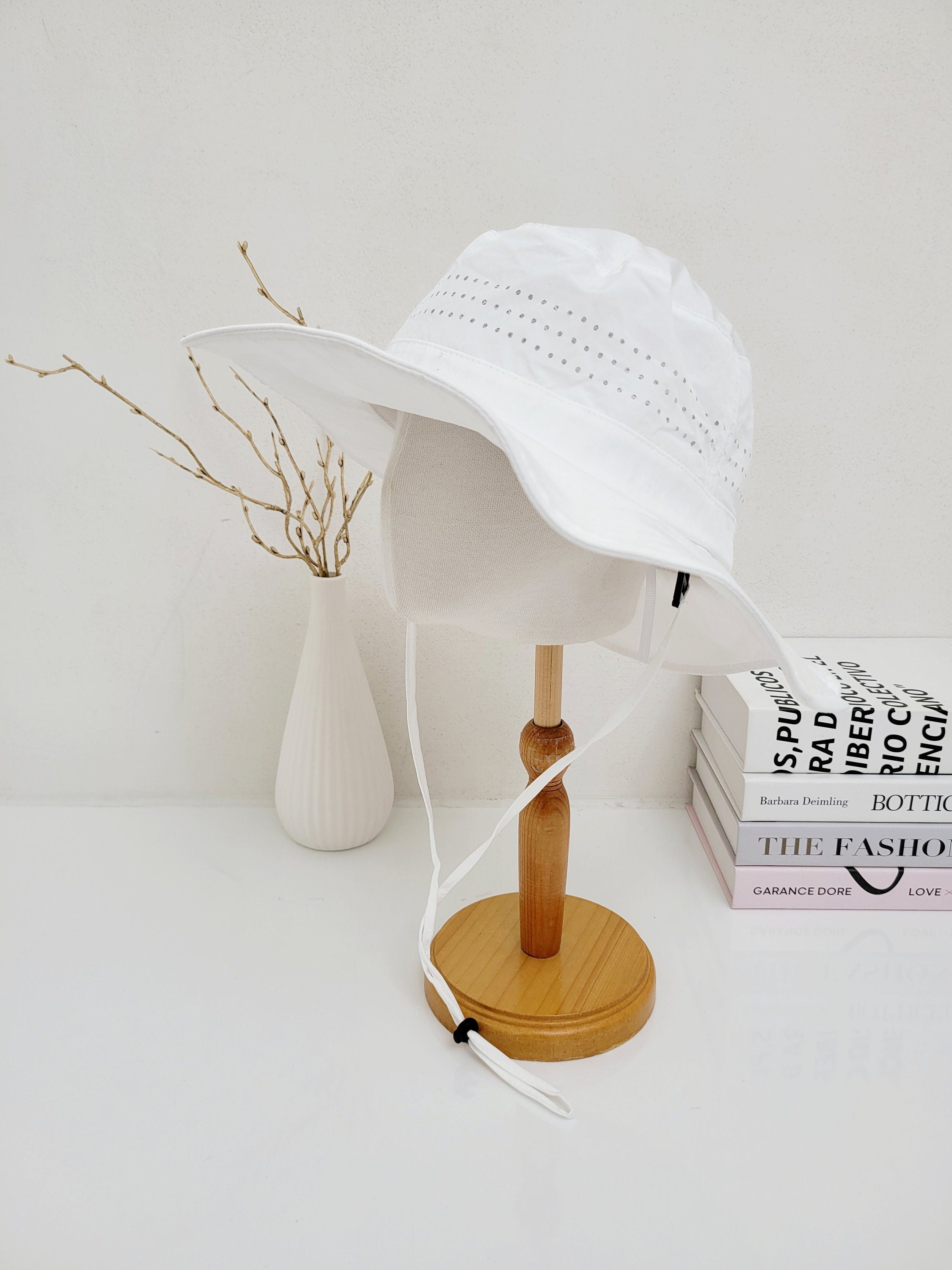 LONG JOURNEY white sun hat with wide brim, ventilation holes, and adjustable chin strap, displayed on a stand.