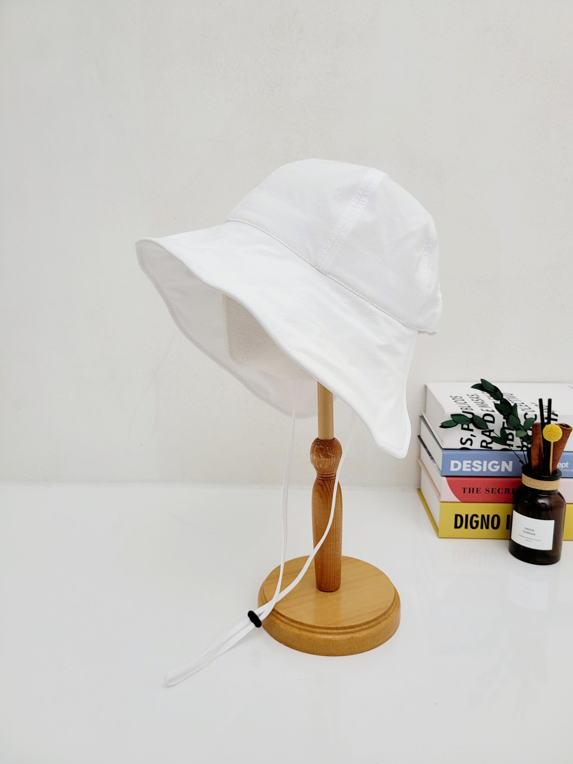 White SUMMER LARGE BRIM HAT on a wooden stand, featuring a wide brim and adjustable chin strap.