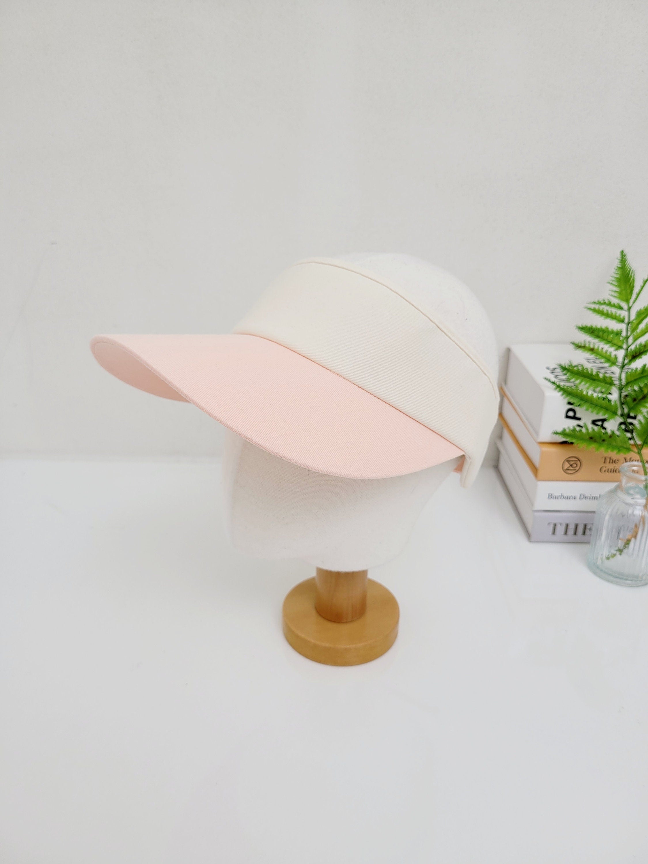White sports sun visor with a pink brim, displayed on a mannequin head. Perfect for outdoor activities.