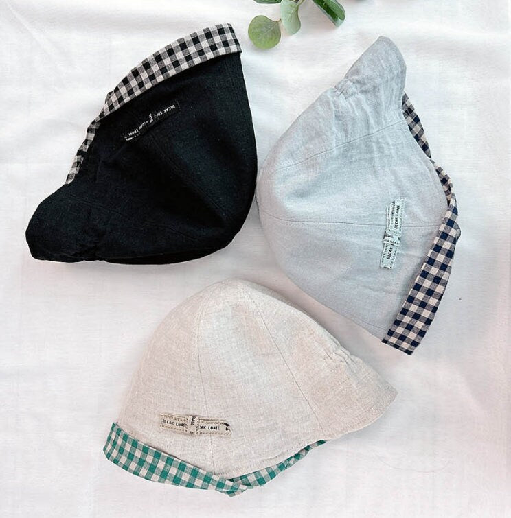Three linen checkered baby sun hats: black, light gray, and off-white, each with a contrasting checkered brim.