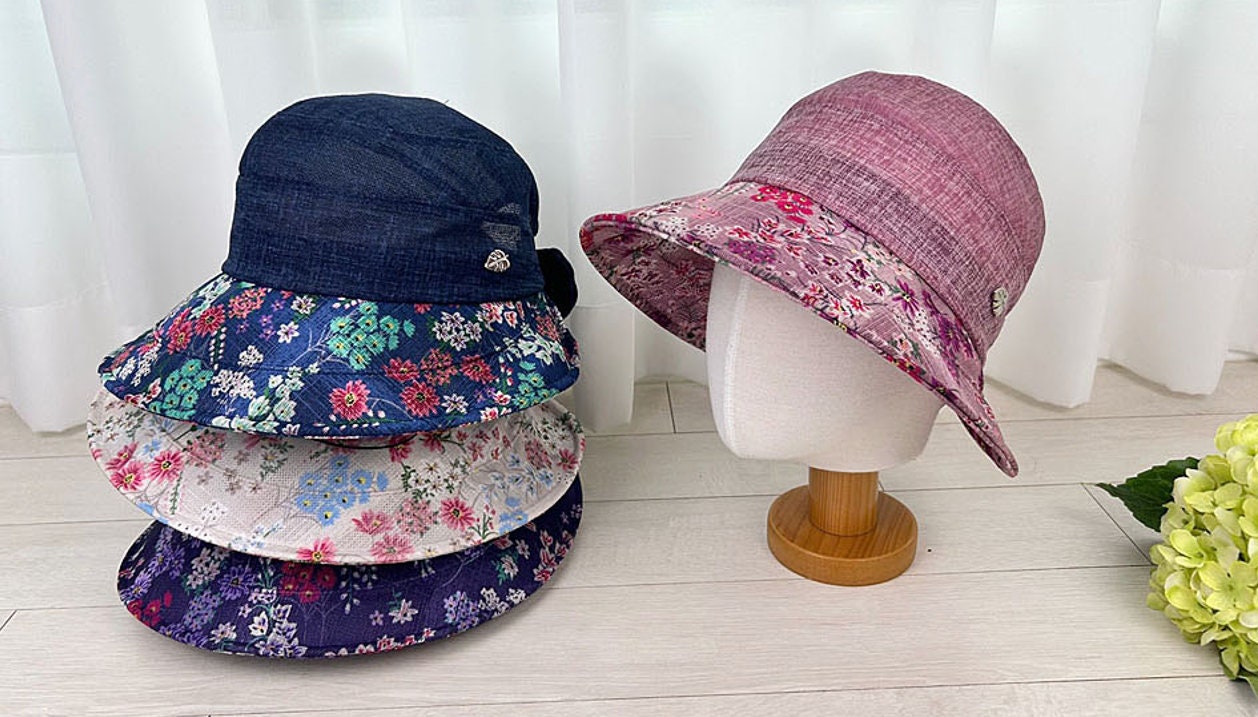 FLORAL BRIM SUMMER HAT: Stack of summer hats with floral patterns, including a pink hat on a mannequin head displaying the hat's brim design.