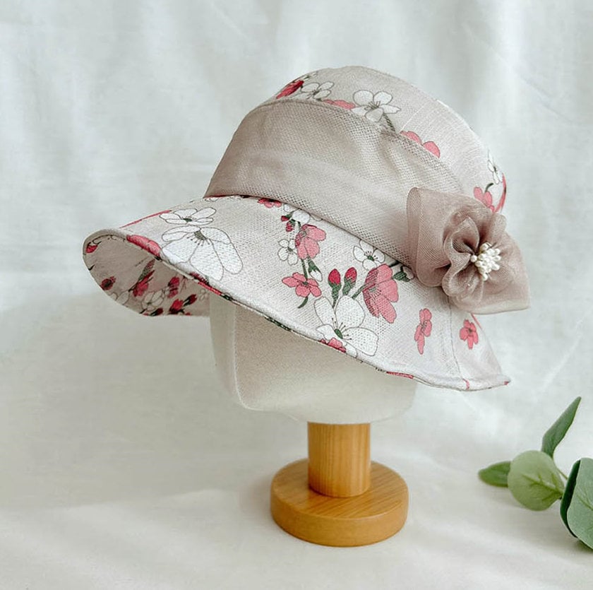 queens summer floral sun hat featuring a wide brim, delicate pink and white flower pattern, sheer ribbon accent, and pearl-centered flower detail. Perfect women's garden hat.