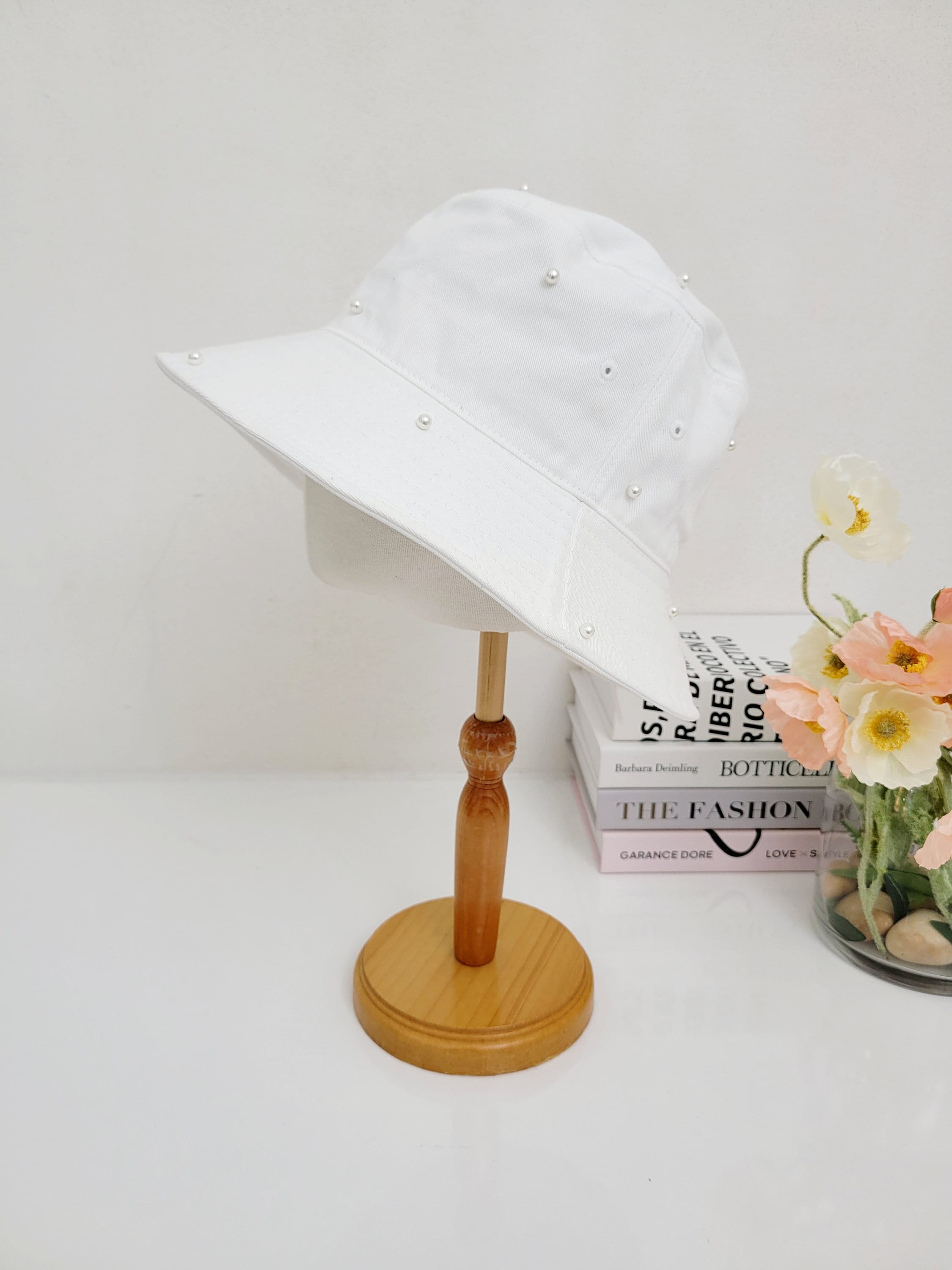 White cotton bucket hat-pearl, adorned with delicate pearl embellishments, displayed on a wooden stand.