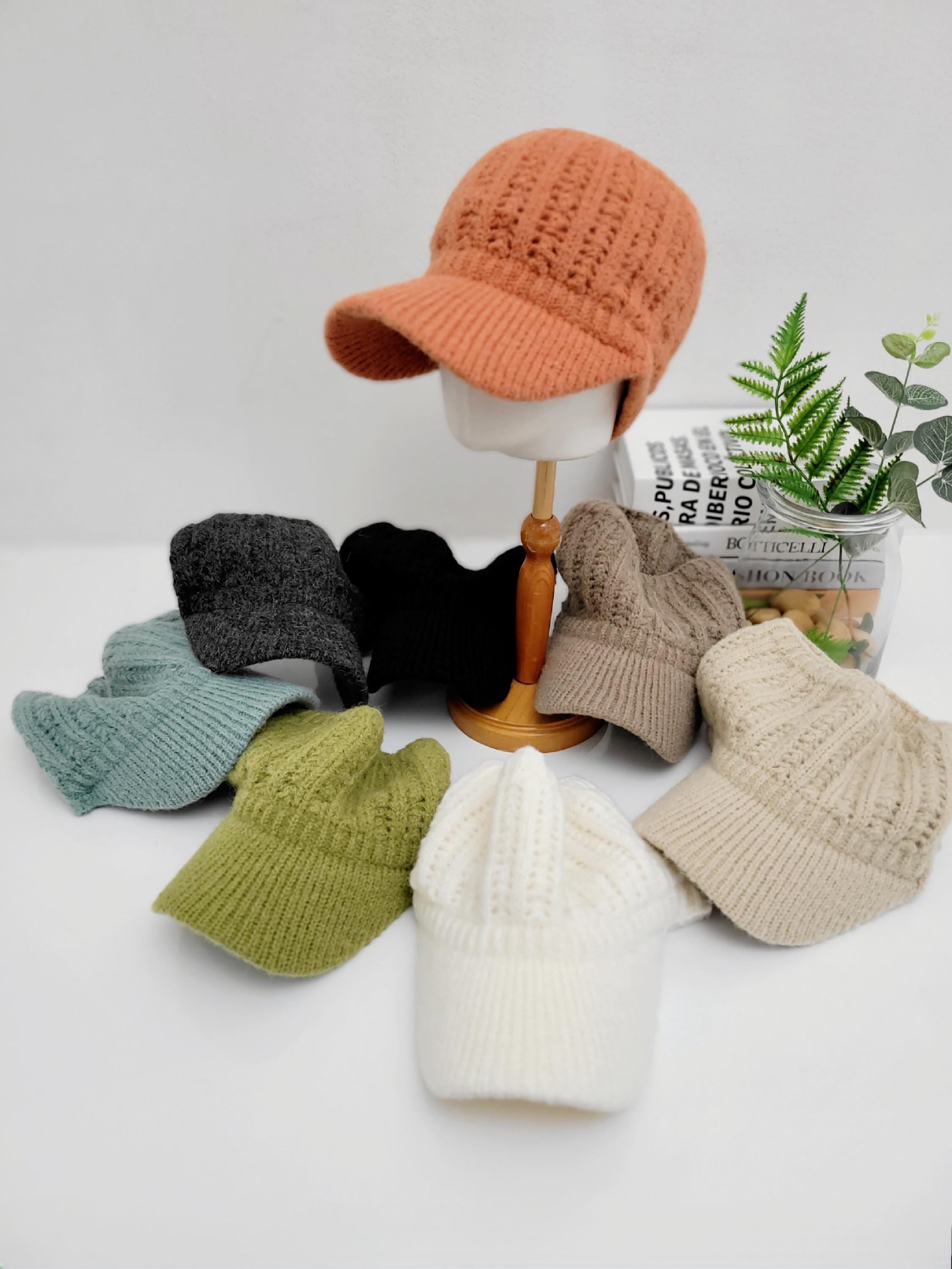 
Crochet baseball cap collection: textured knit caps in orange, gray, black, beige, green, light blue, and white, displayed on a white surface with a book and plant.
