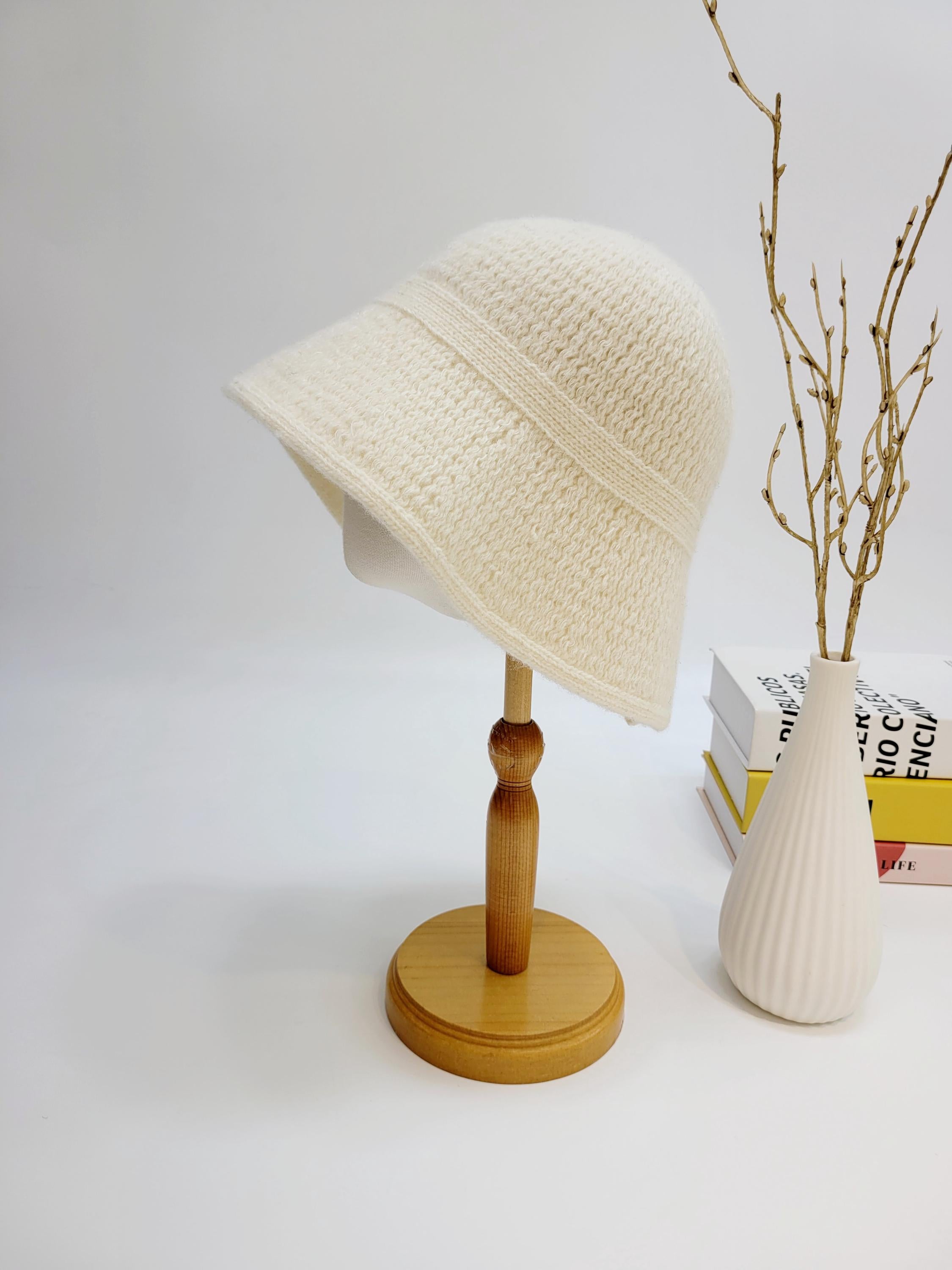 Cream-white knitted victoria's winter hat on a wooden stand, showcasing its soft texture and classic bucket shape.