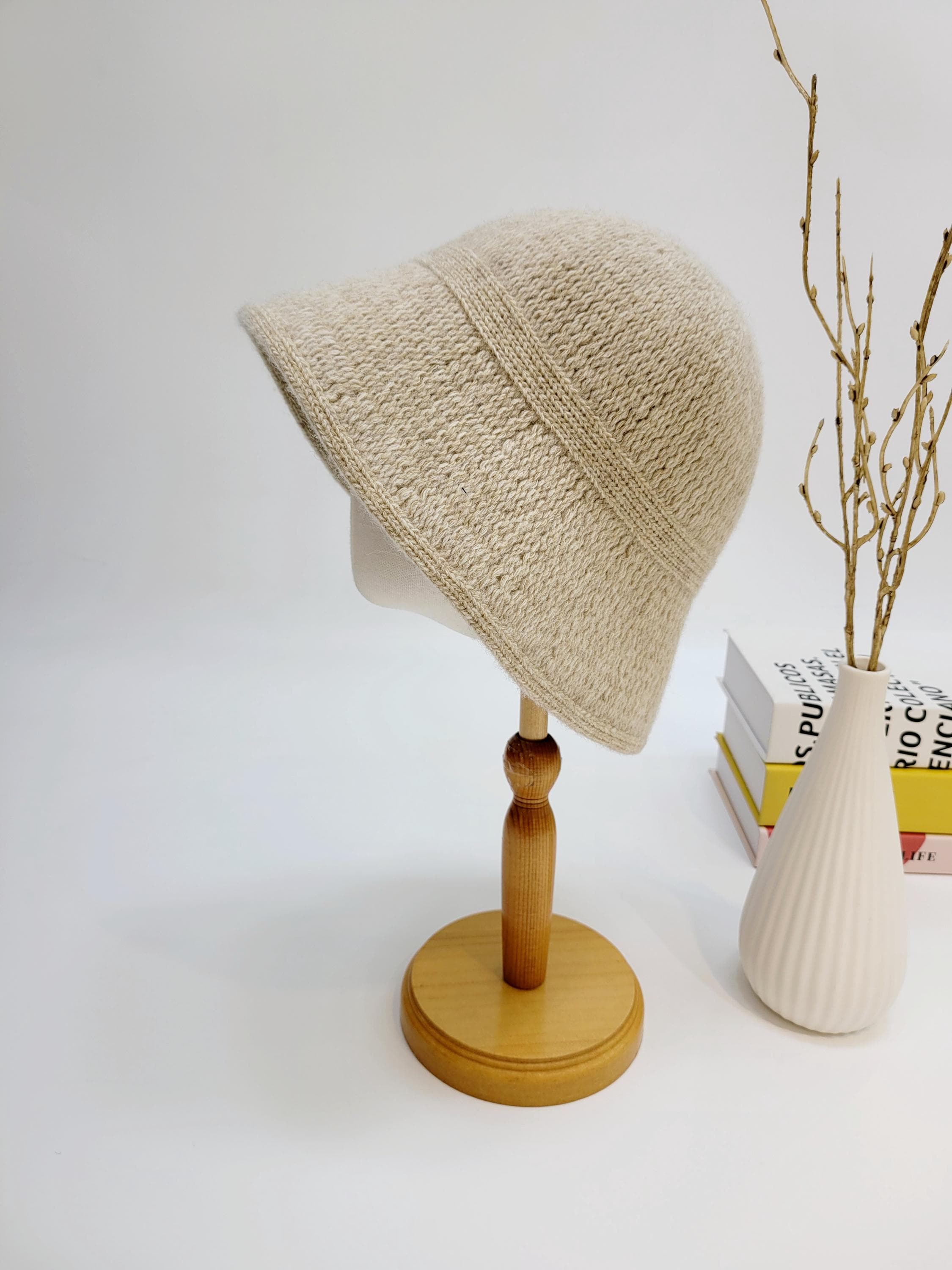 Beige knitted victoria's winter hat on a stand. A cozy, neutral-toned bucket hat, perfect for winter warmth.