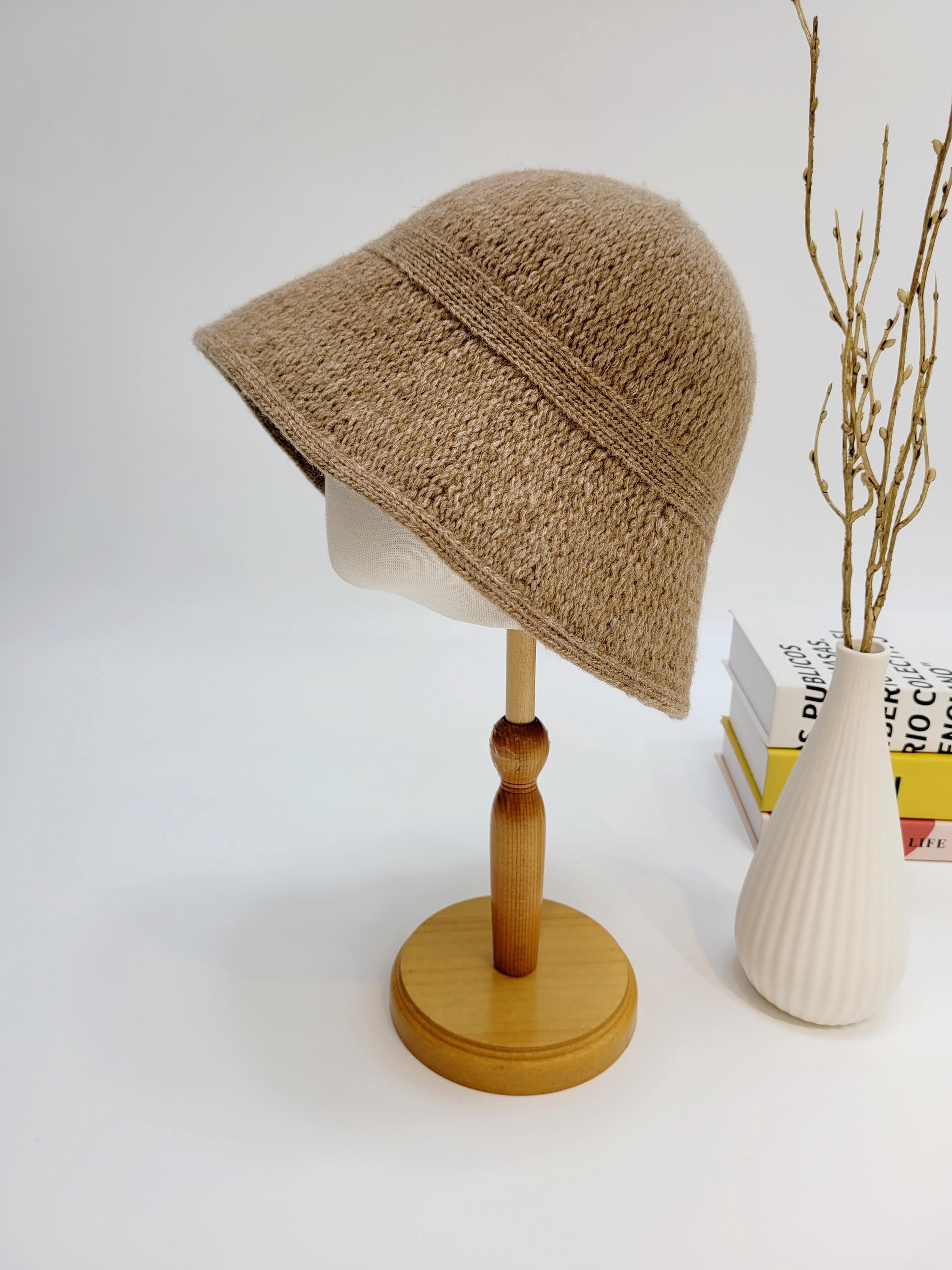 Knitted brown victoria's winter hat on a wooden stand, showcasing its texture and brim shape.