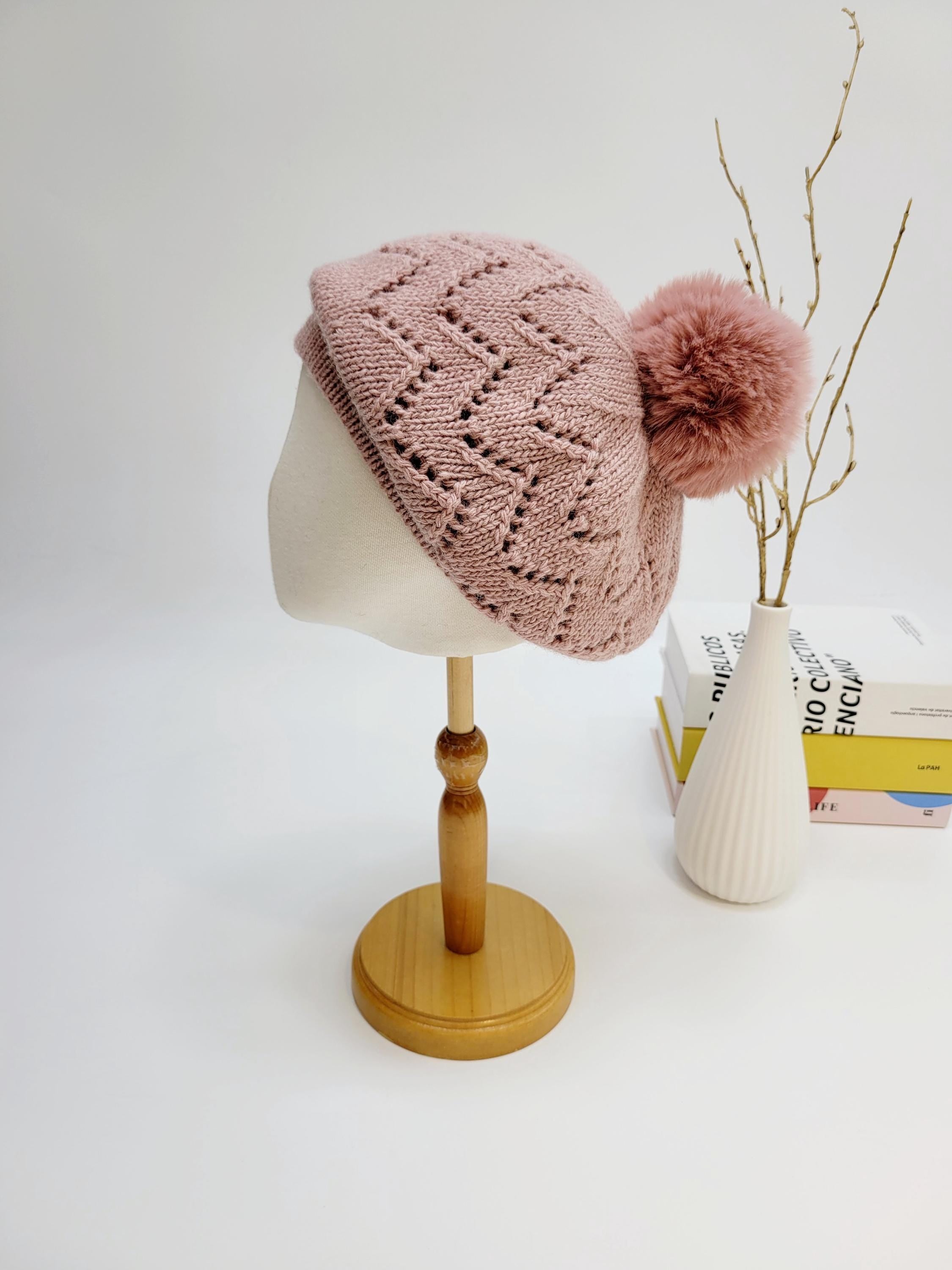 Pink knitted beret with lacy design and fluffy pompom, from emma in paris, displayed on a mannequin head.