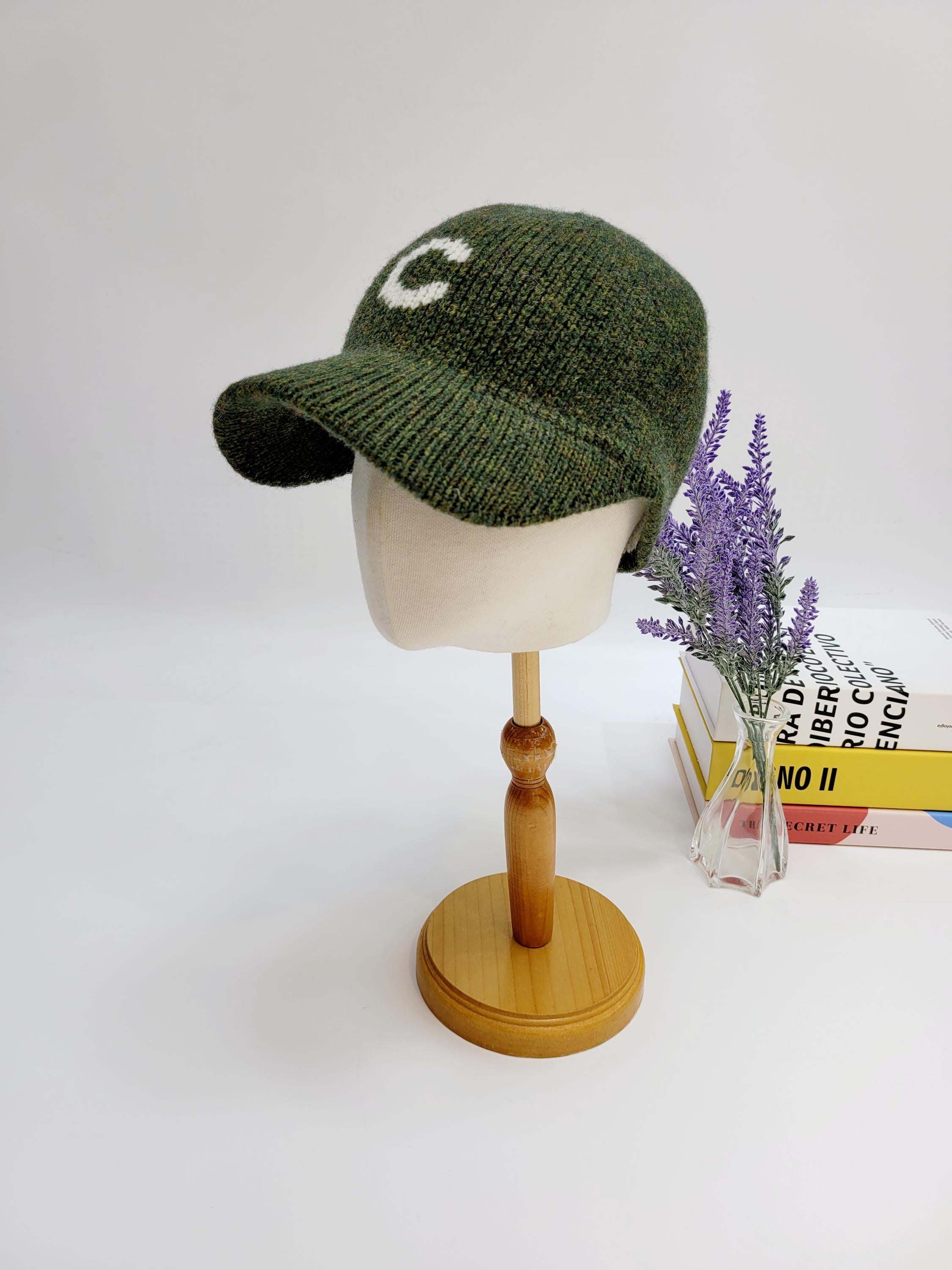 Green c-wool cap on a mannequin head, featuring a white "C" knit on the front. A stylish and cozy hat.