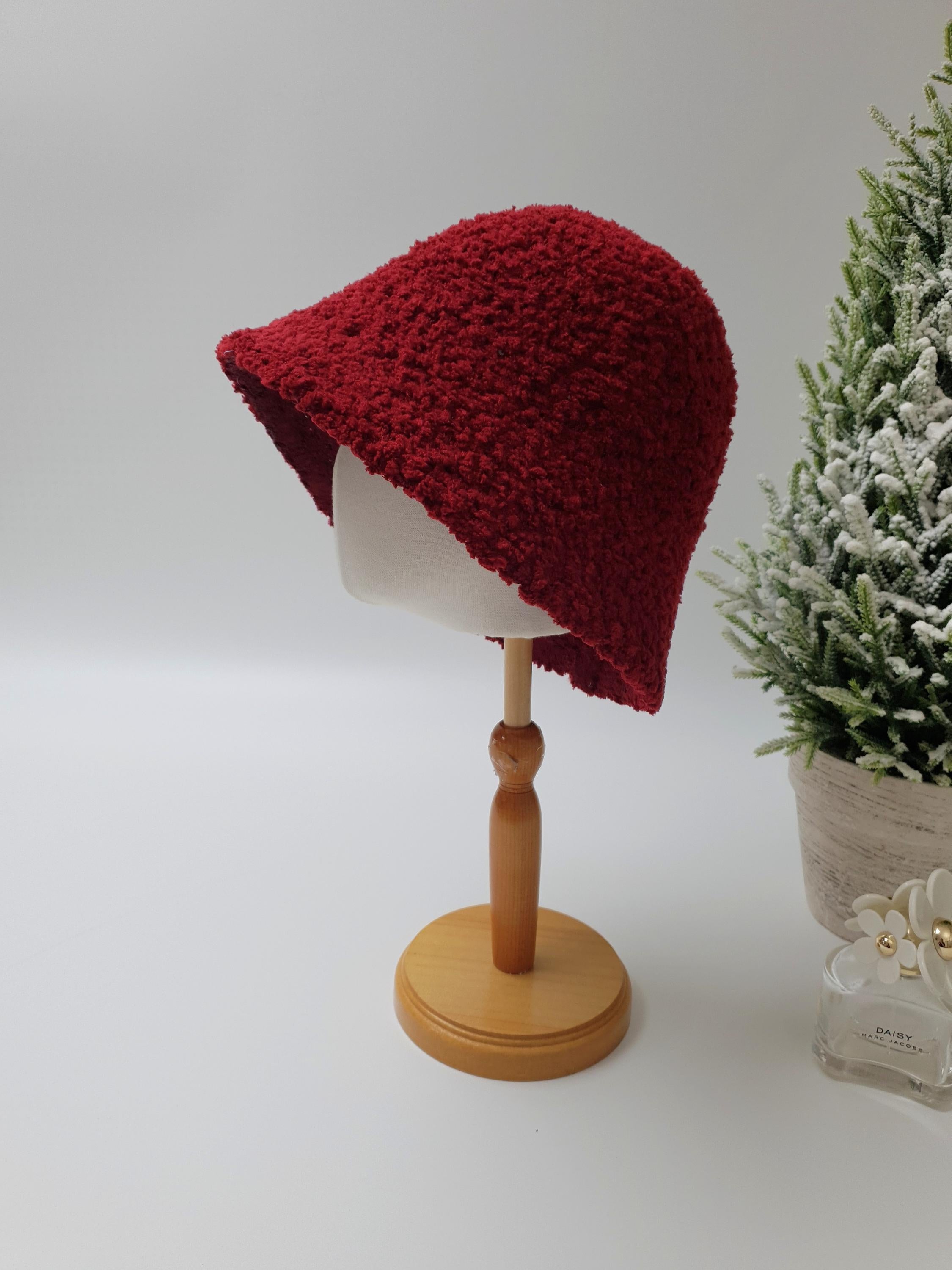 Red sherpa bucket hat on a wooden stand. Soft, textured sherpa fabric gives this sherpa bucket hat a cozy, warm look.
