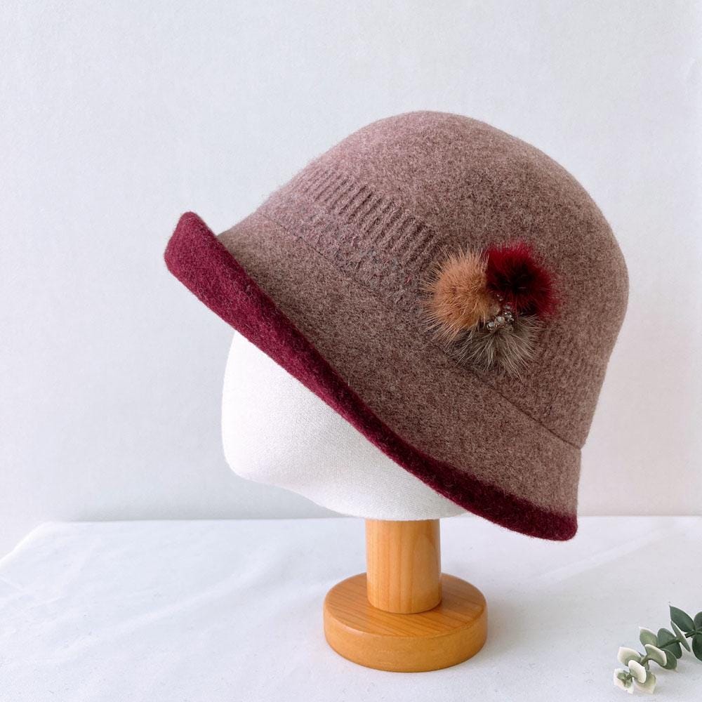 Wool my first lady hat in mauve with burgundy brim, accented by a fluffy pompom detail. Stylish and warm.