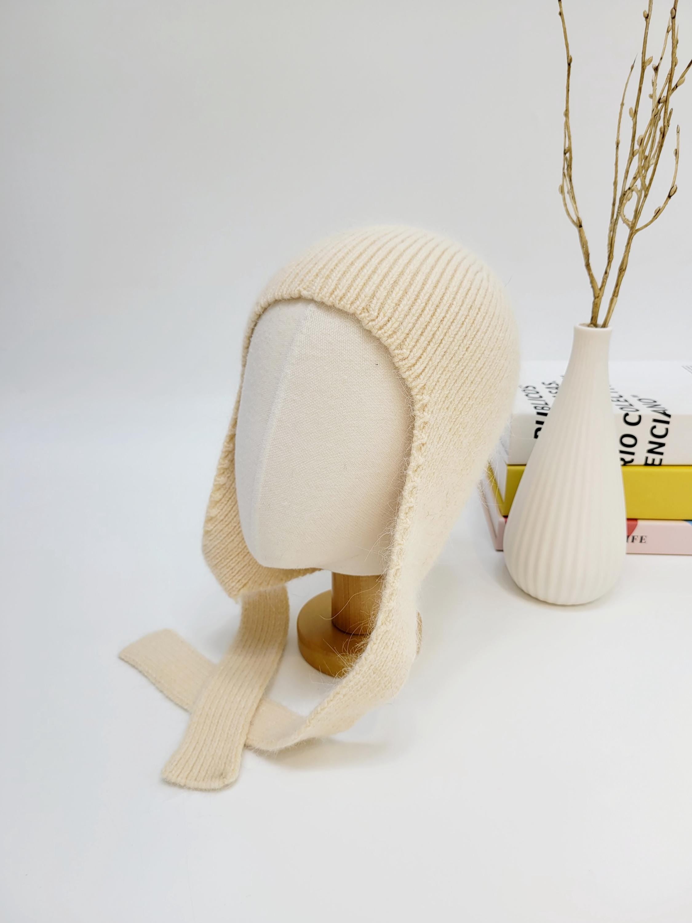 Cream wool balaclava on mannequin, featuring soft knit texture and tie closures, offering warmth and style.