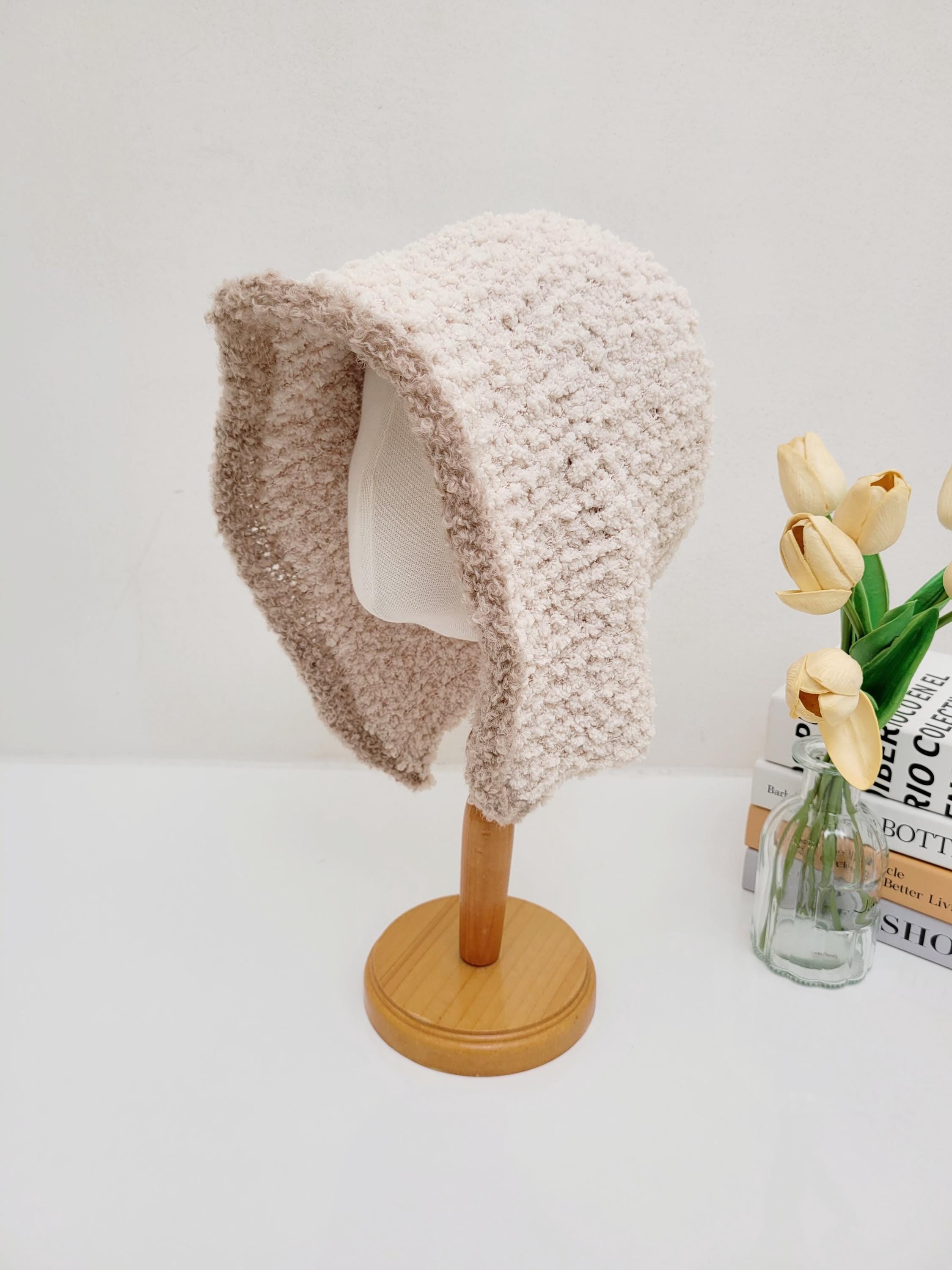 Beige wool hooded hat on a wooden stand, soft texture, cozy design.