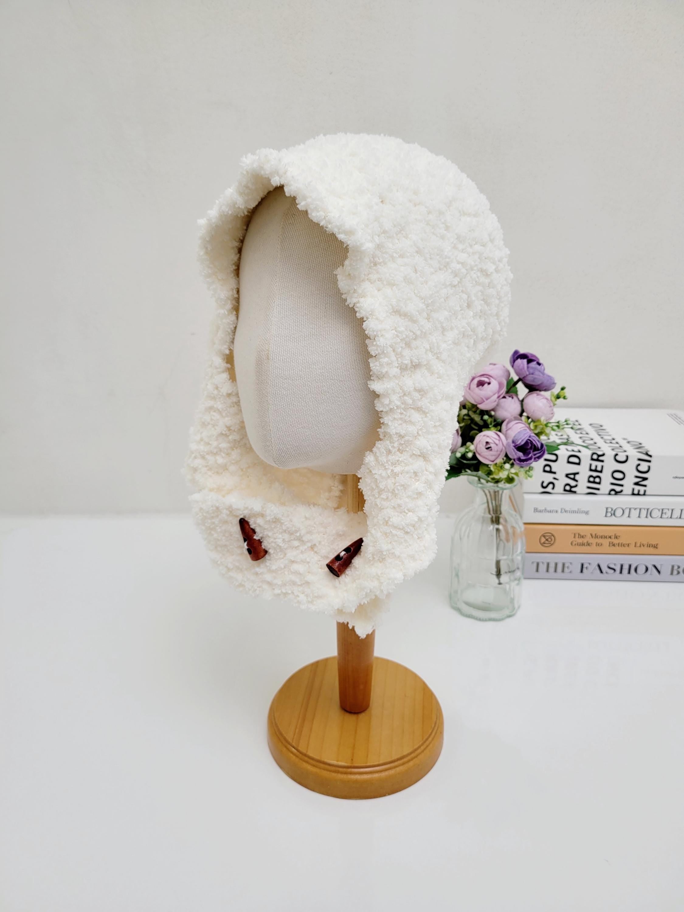 fluffy balaclava in soft white fabric displayed on a mannequin head, featuring small brown accents at the front
