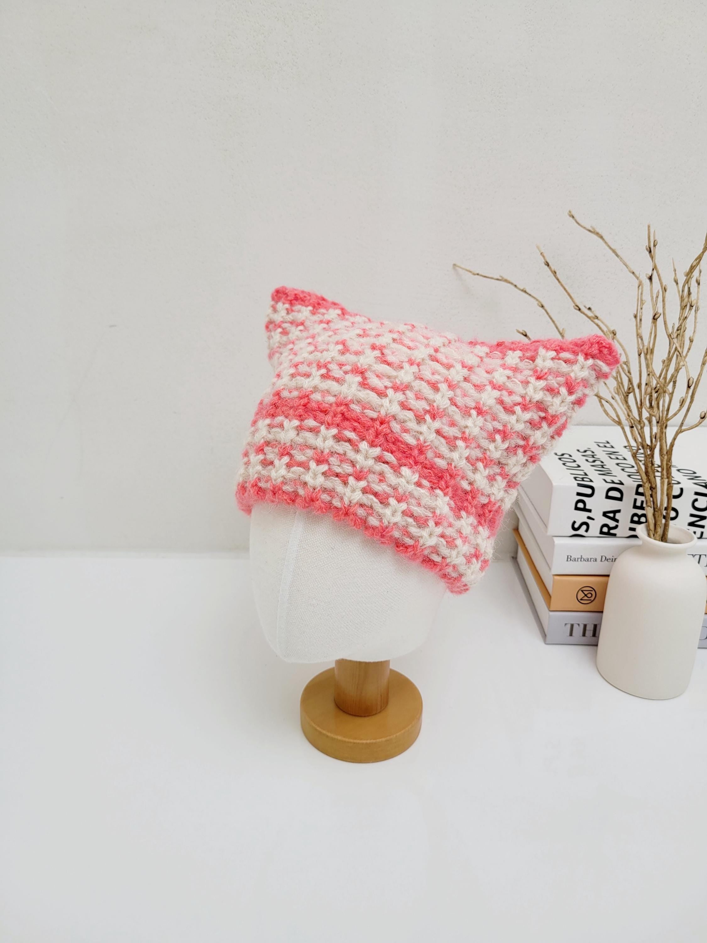 Pink and white knitted cat ear hat on a mannequin head. The hat has pointed ears and a chunky knit texture.