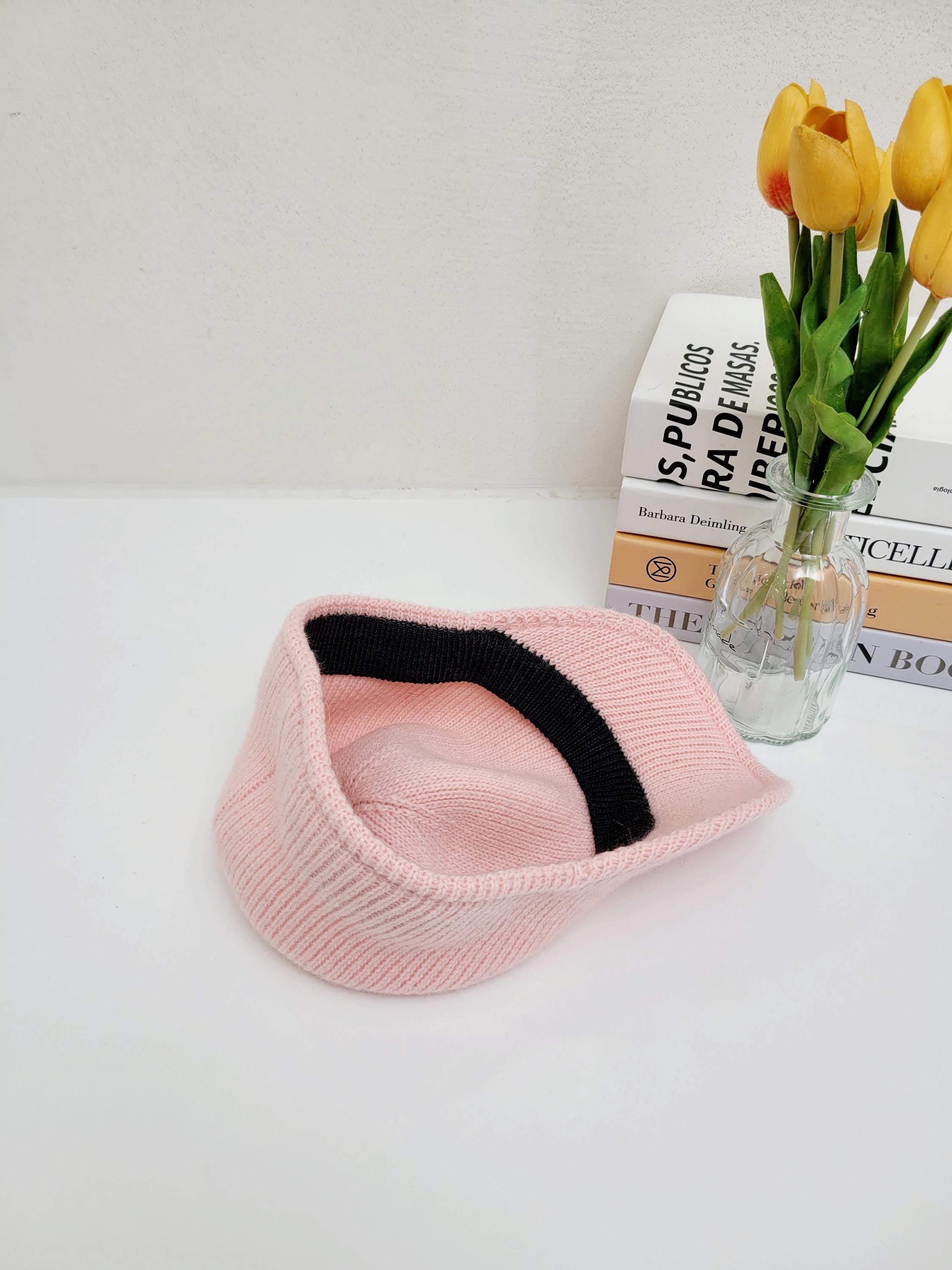 Pink ribbed cap with a black inner band, lying on a white surface. Stylish and comfortable headwear.