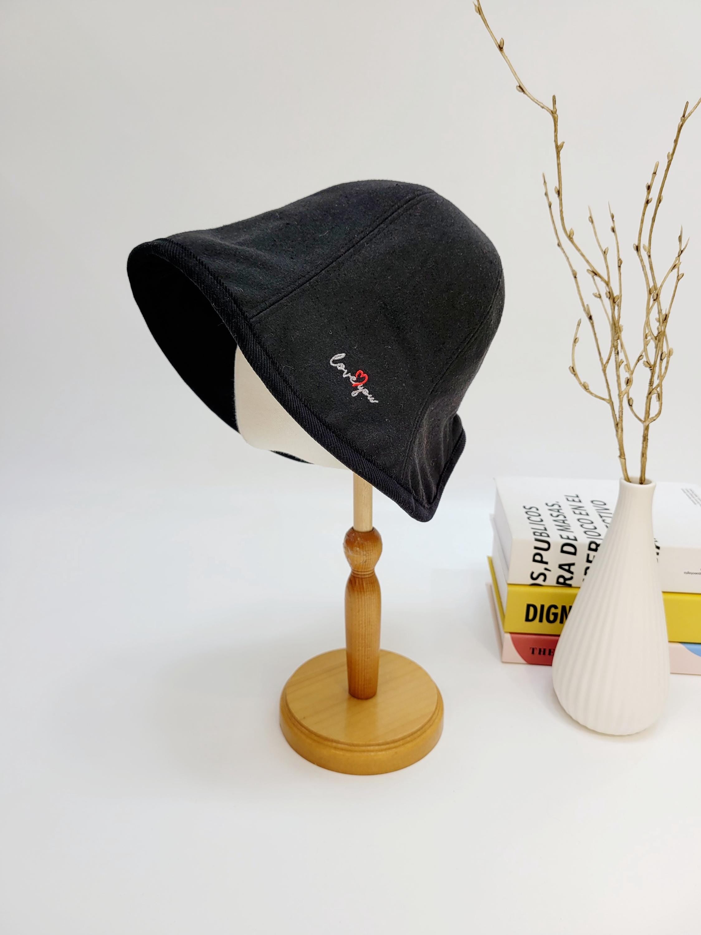 Black wool bucket hat with "love you" embroidery detail, displayed on a wooden stand