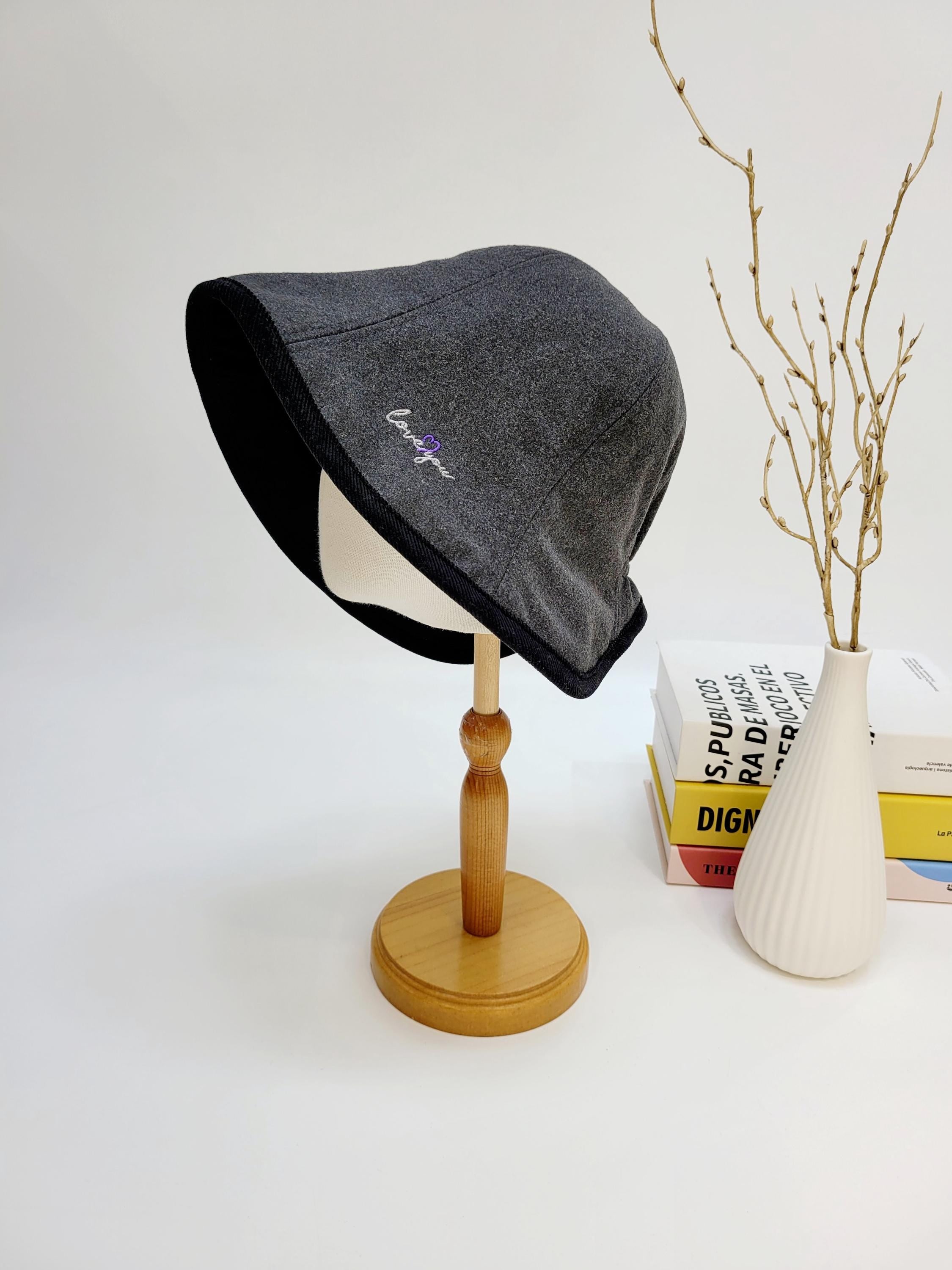 Gray wool hat with black trim and "love you" embroidery, displayed on a wooden stand, a stylish and cozy accessory.