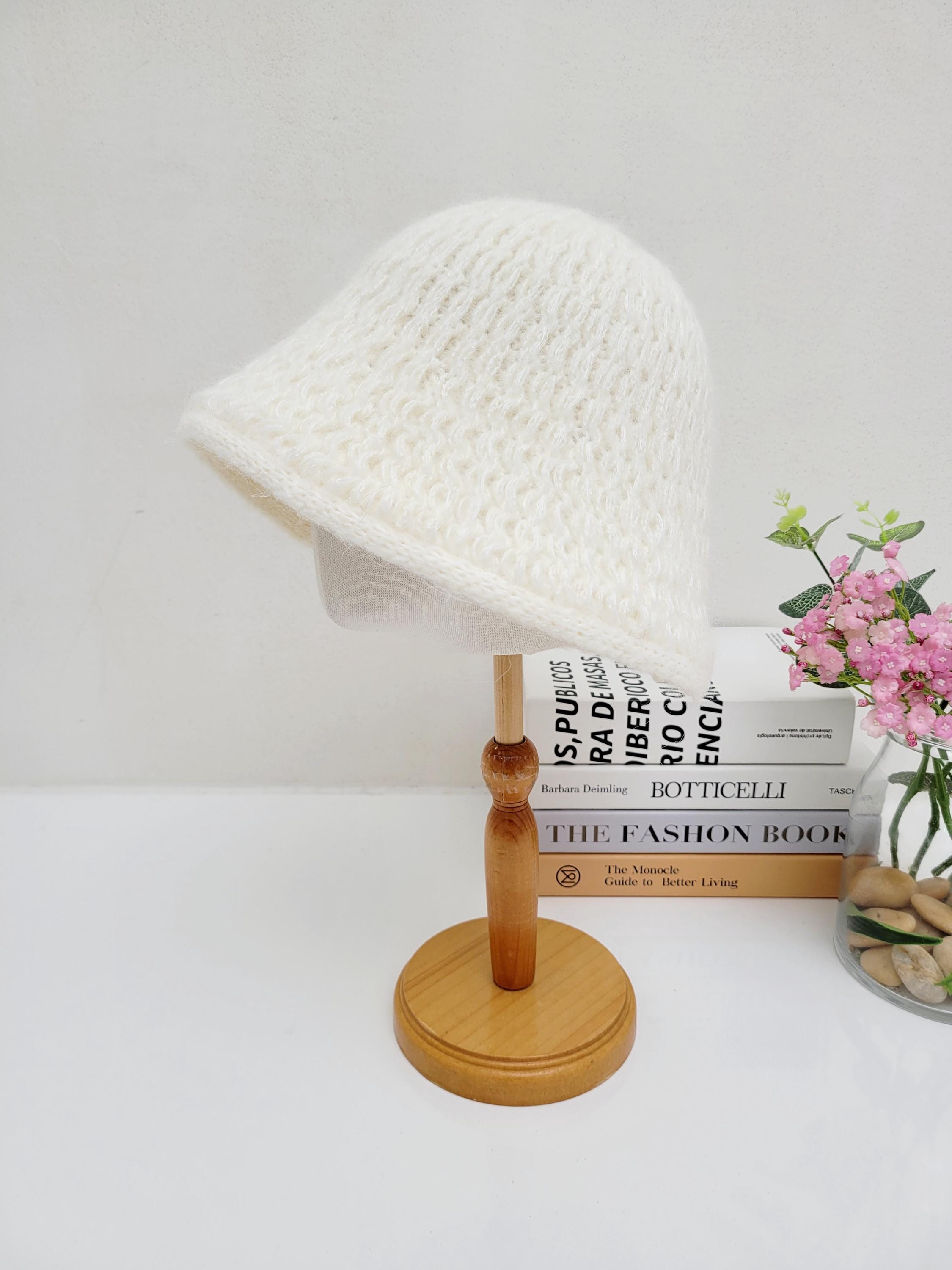 Creamy white wool bucket hat on a wooden stand; soft, textured knit design with a subtle brim.