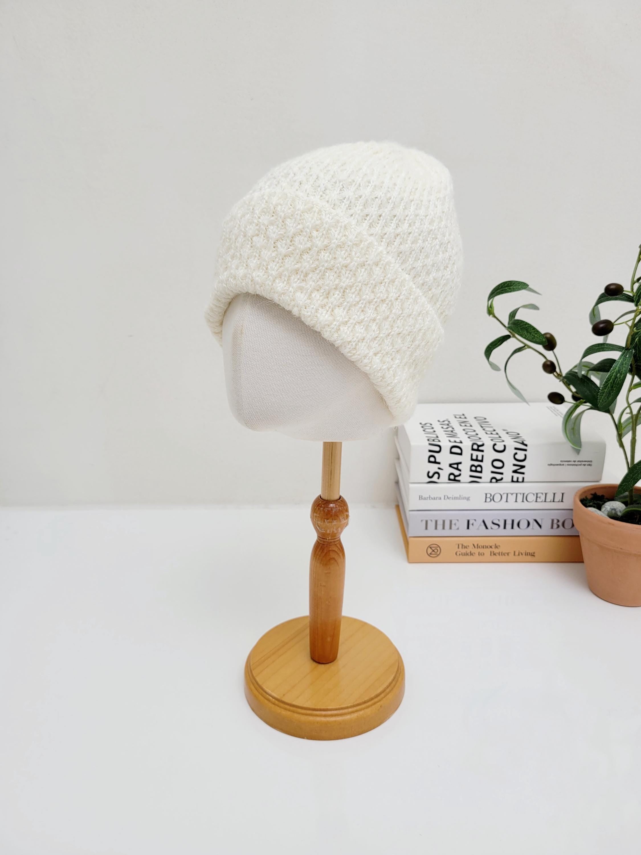 Cream-colored knit TAYLOR beanie on a wooden display stand. Soft, textured knit with a folded brim.