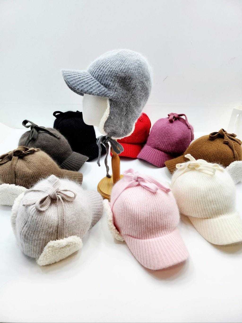 Angora trapper earflap hats in assorted colors: gray, black, red, pink, brown, and cream. Each hat features soft earflaps and a tie closure.