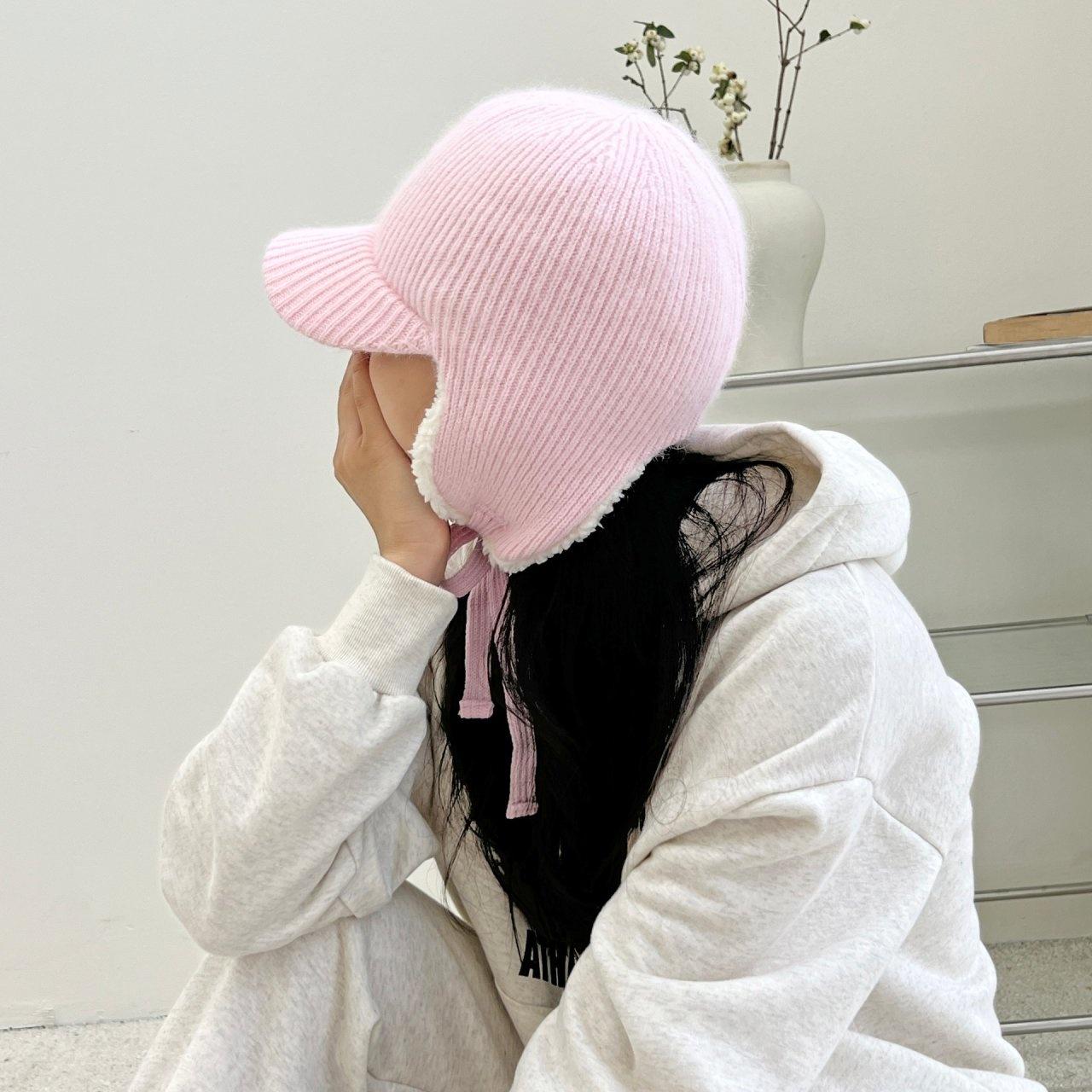 Pink angora trapper earflap hat with soft white lining and tie closures, worn with a casual hooded sweatshirt.