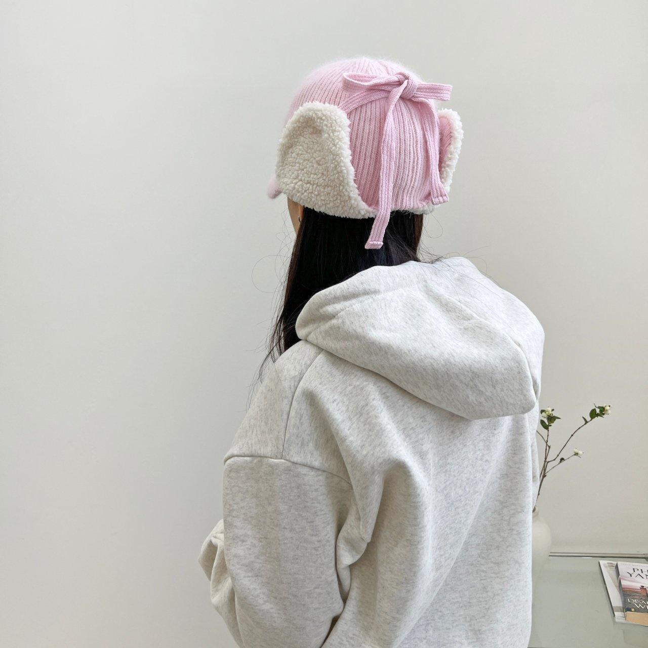 
angora trapper - earflap in baby pink knit with faux shearling ear flaps and tie detail, seen from the back on a person wearing a gray hoodie.
