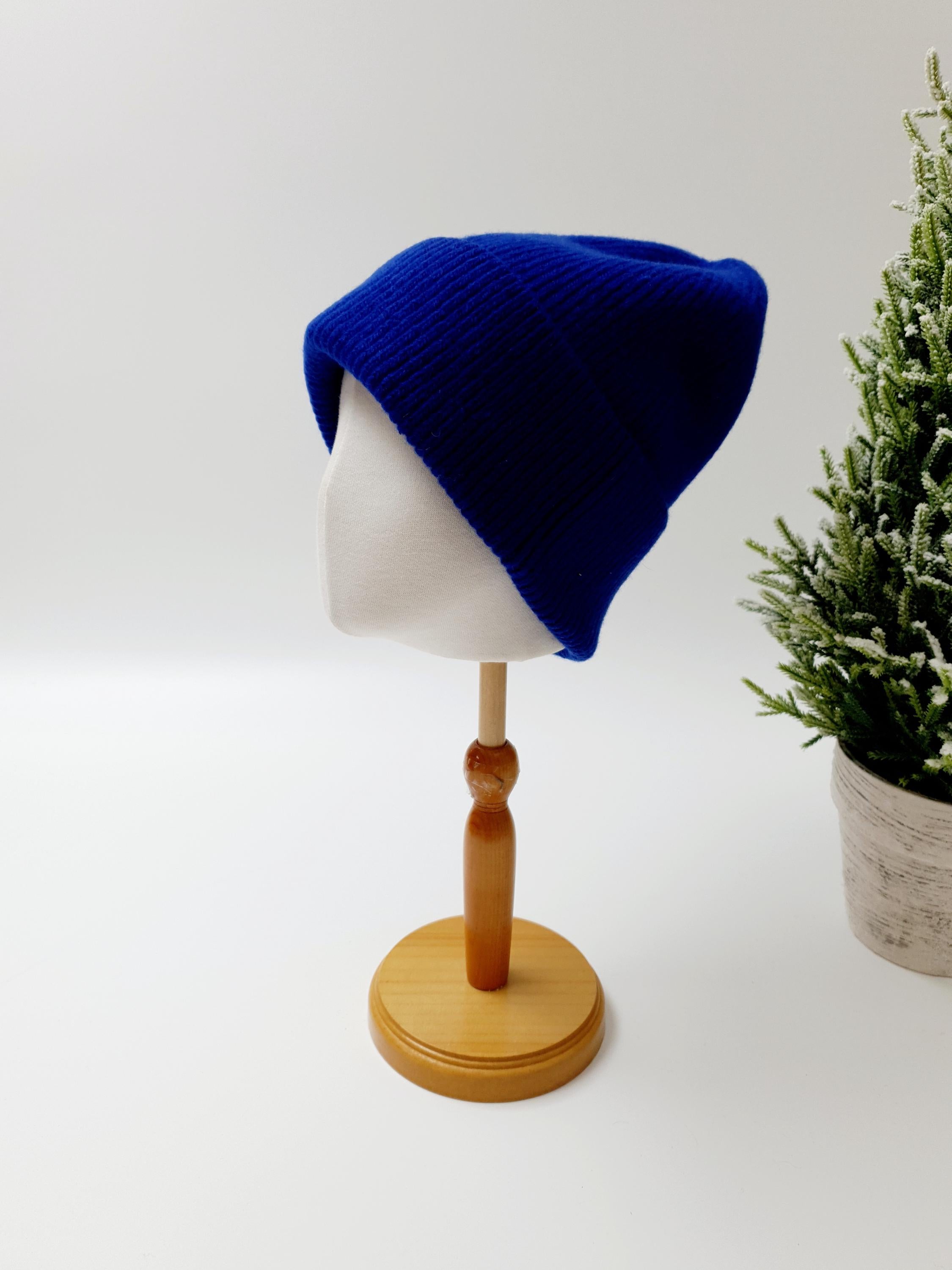 Royal blue knit beanie the wool on a wooden display stand; a cozy and stylish winter hat.