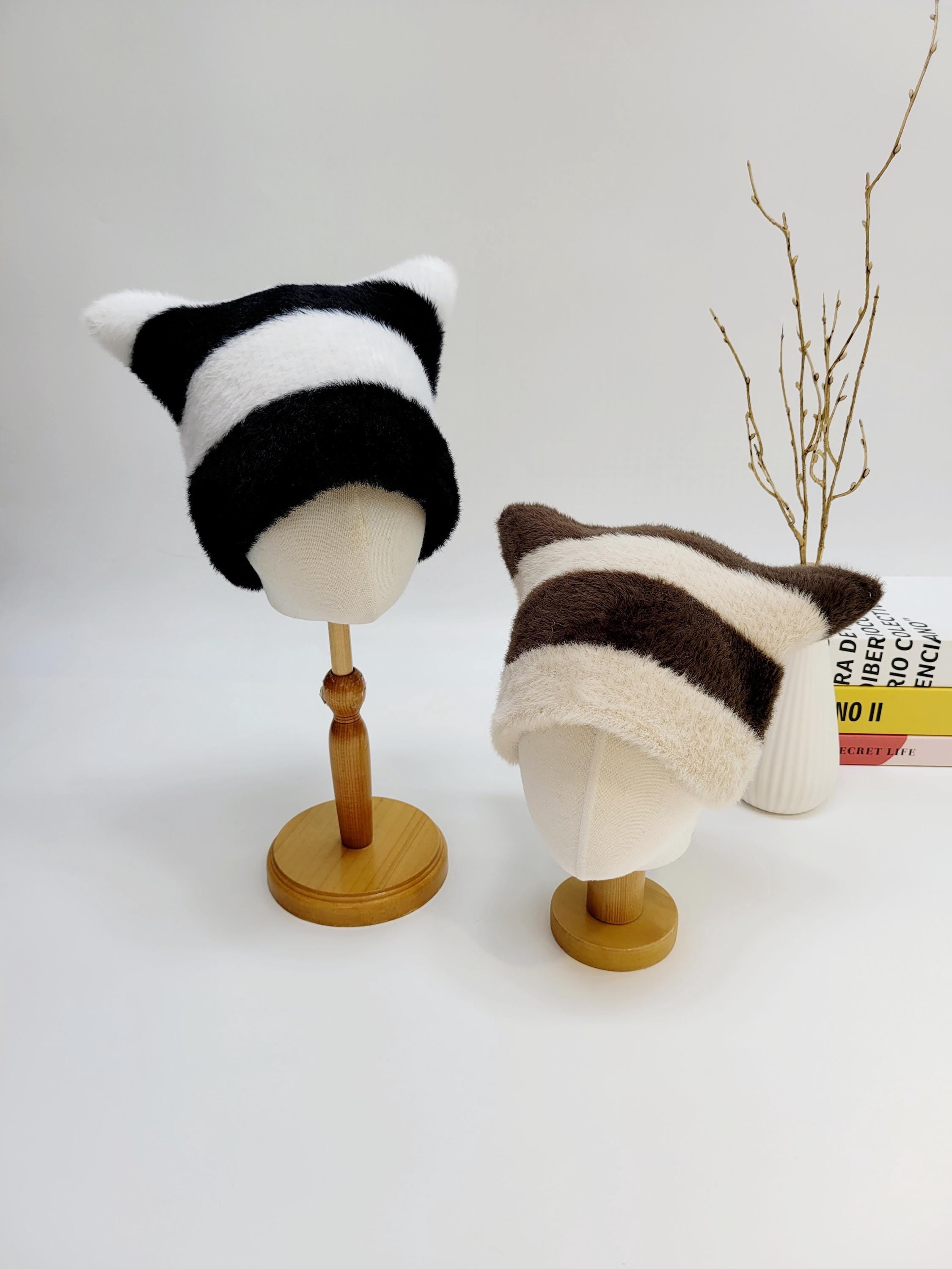 Two cat ear-stripe hats: black/white and brown/cream striped, soft and cozy, displayed on mannequin heads.