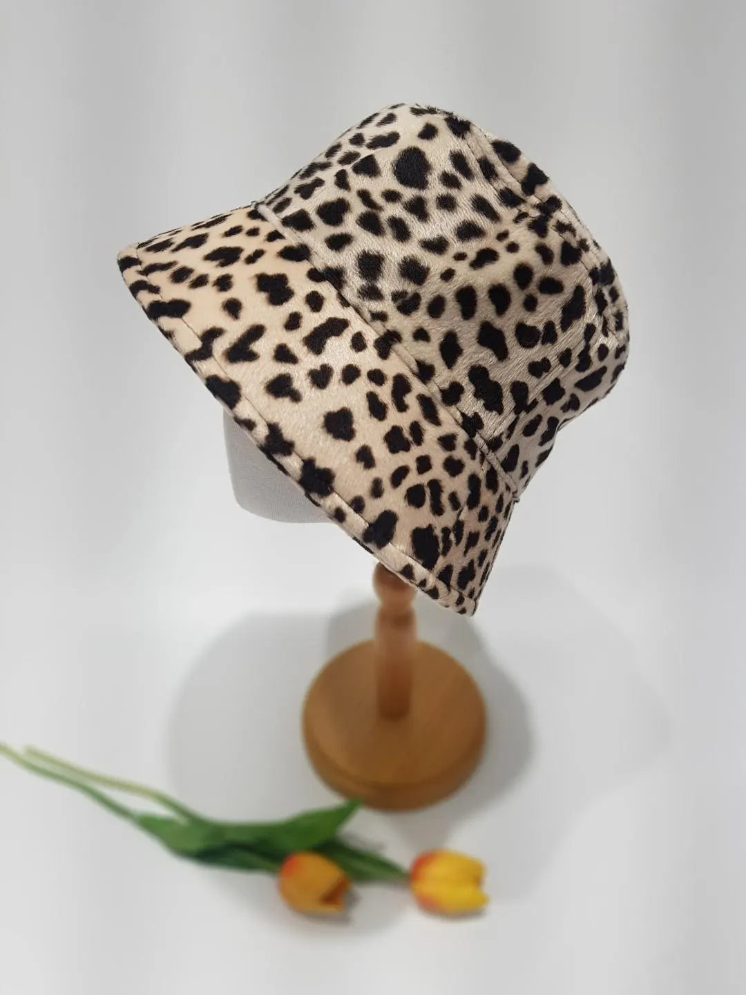 BIG CAT-BUCKET hat in a tan and black leopard print, displayed on a wooden stand. A stylish and trendy statement piece.