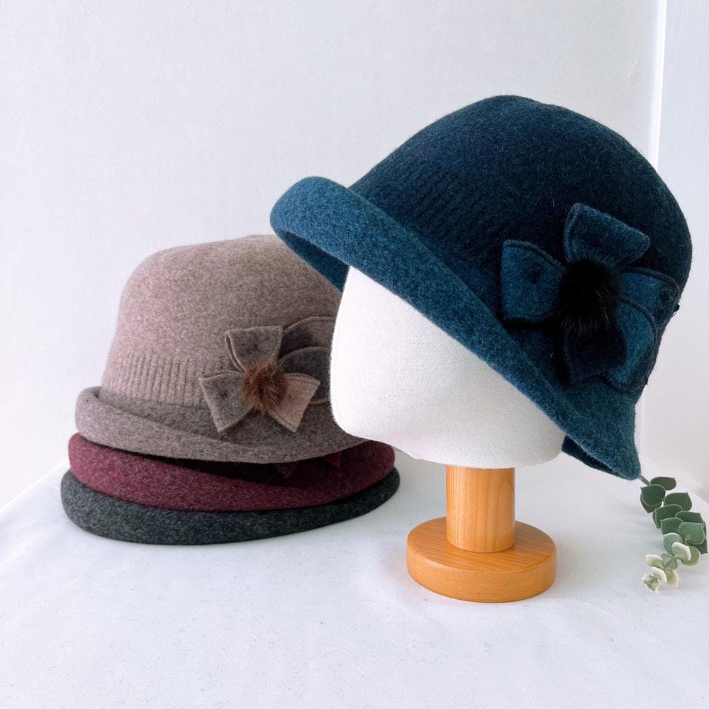 Vintage color wool bucket hat in navy, taupe, and burgundy, each adorned with a charming bow. Navy hat displayed on a stand.