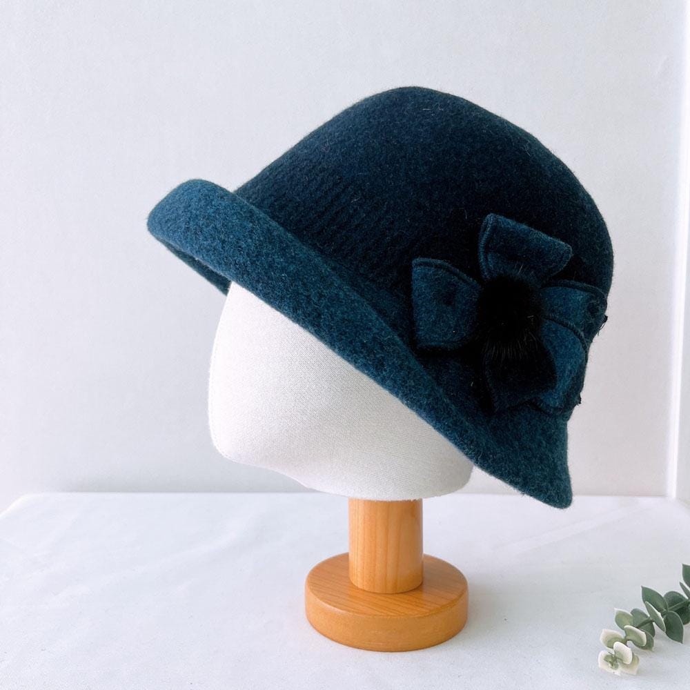 Dark teal vintage color wool bucket hat with flower detail, displayed on a hat stand