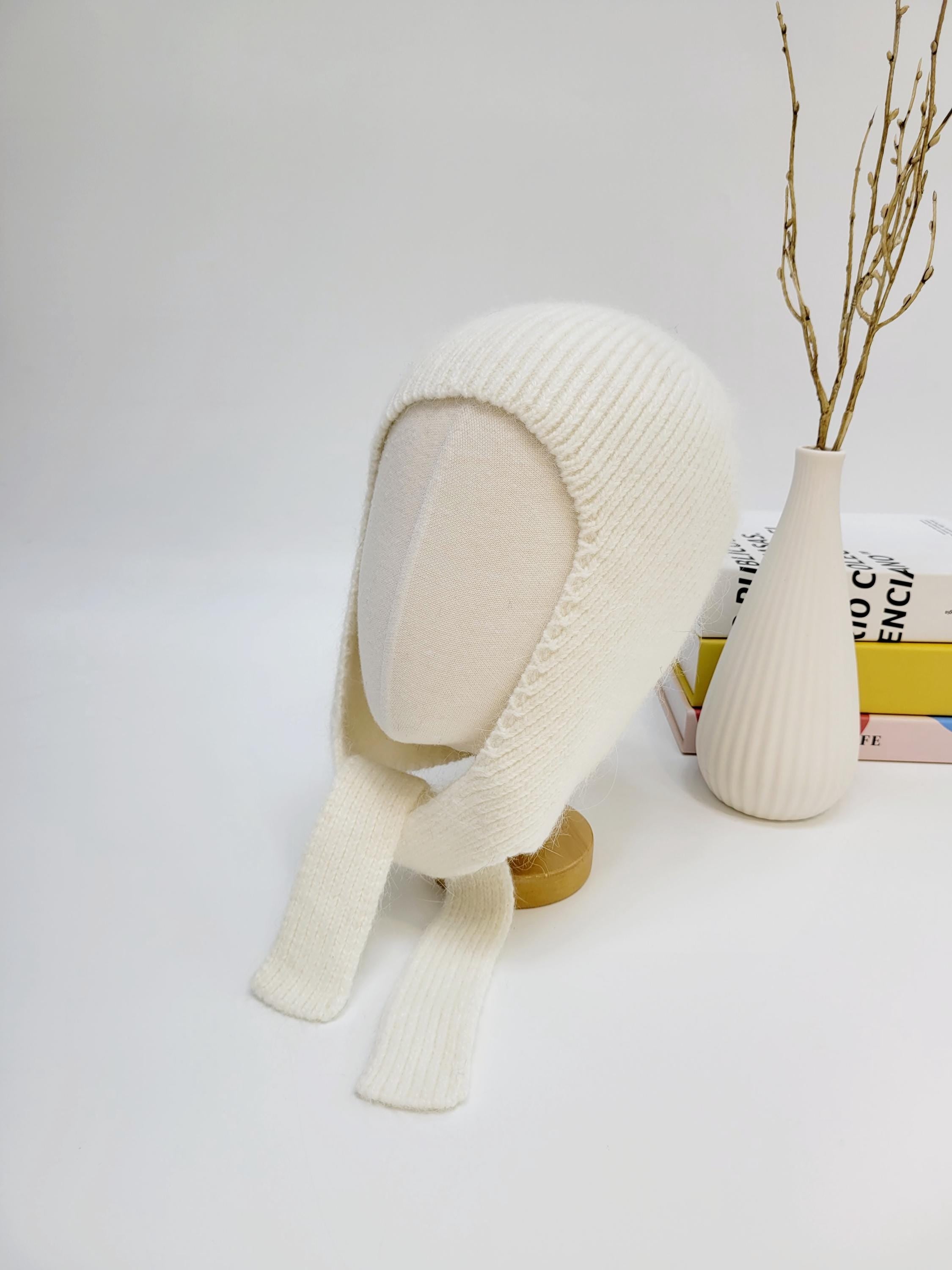 White wool balaclava on a mannequin, featuring a soft knit texture and ear flaps with long ties.