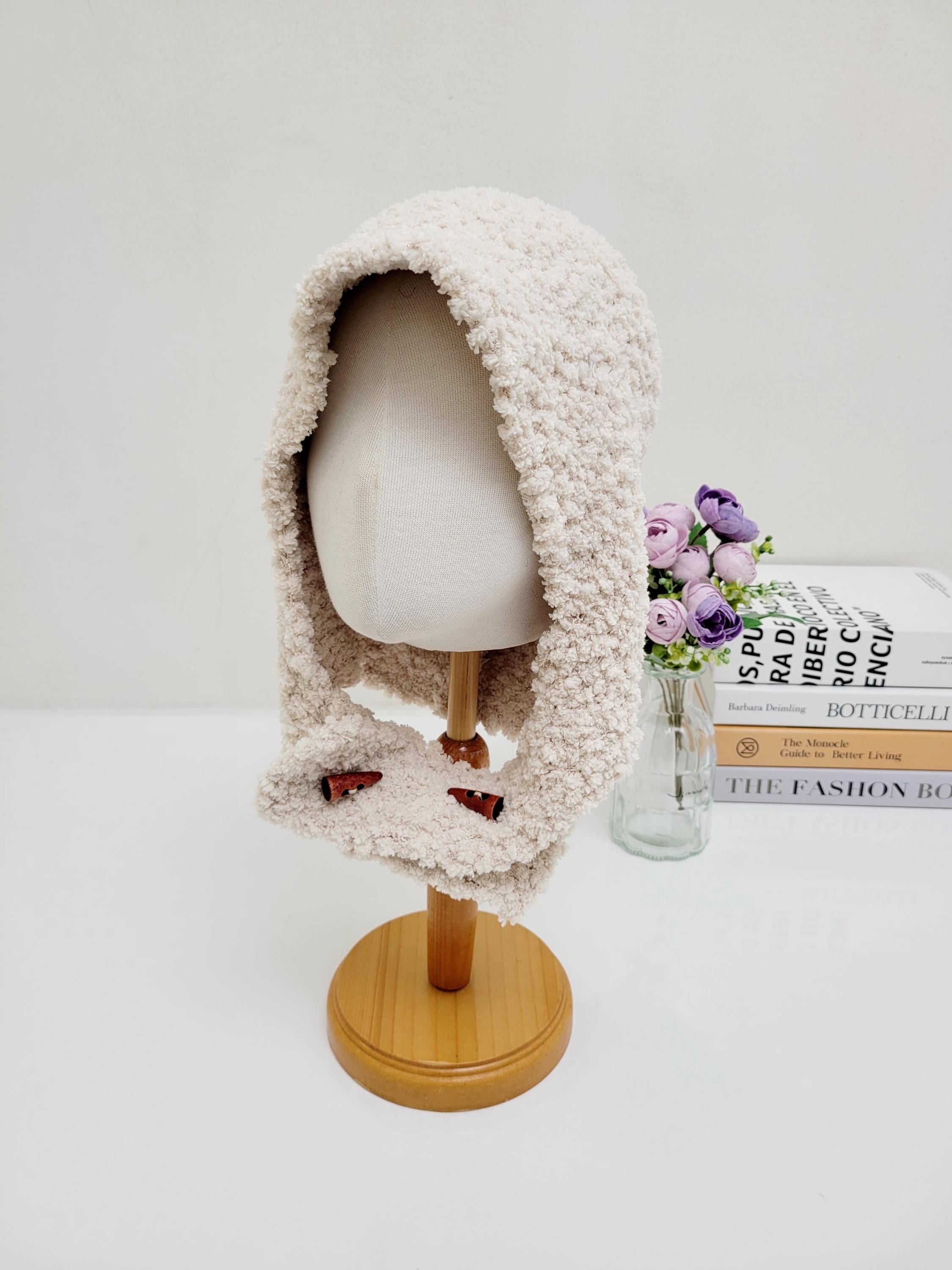 Creamy beige fluffy balaclava on a mannequin, featuring a soft, textured knit and button details. A cozy and stylish headwear option.