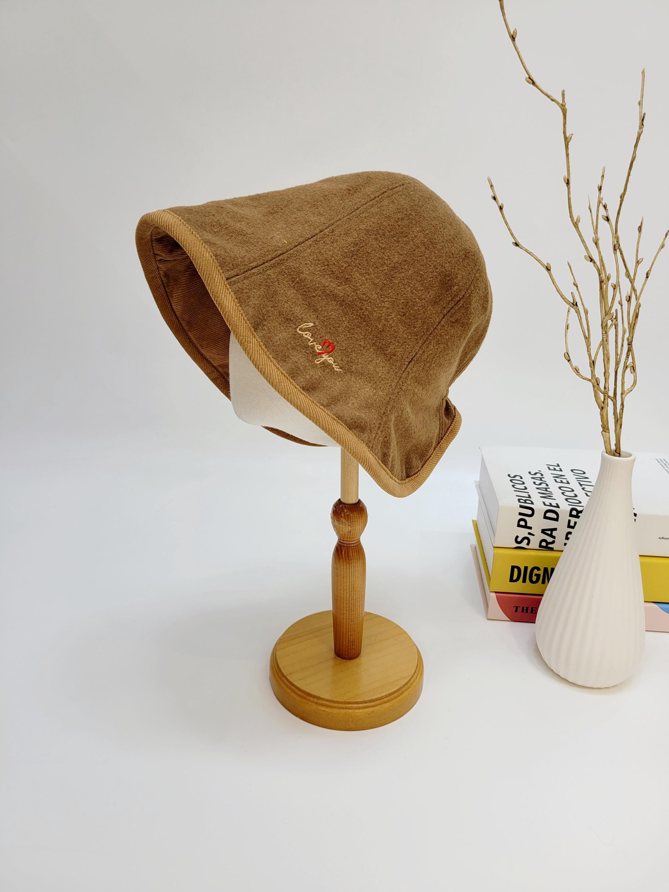 Brown wool bucket hat with "love you" embroidery detail, displayed on a wooden stand. A stylish and cozy accessory.