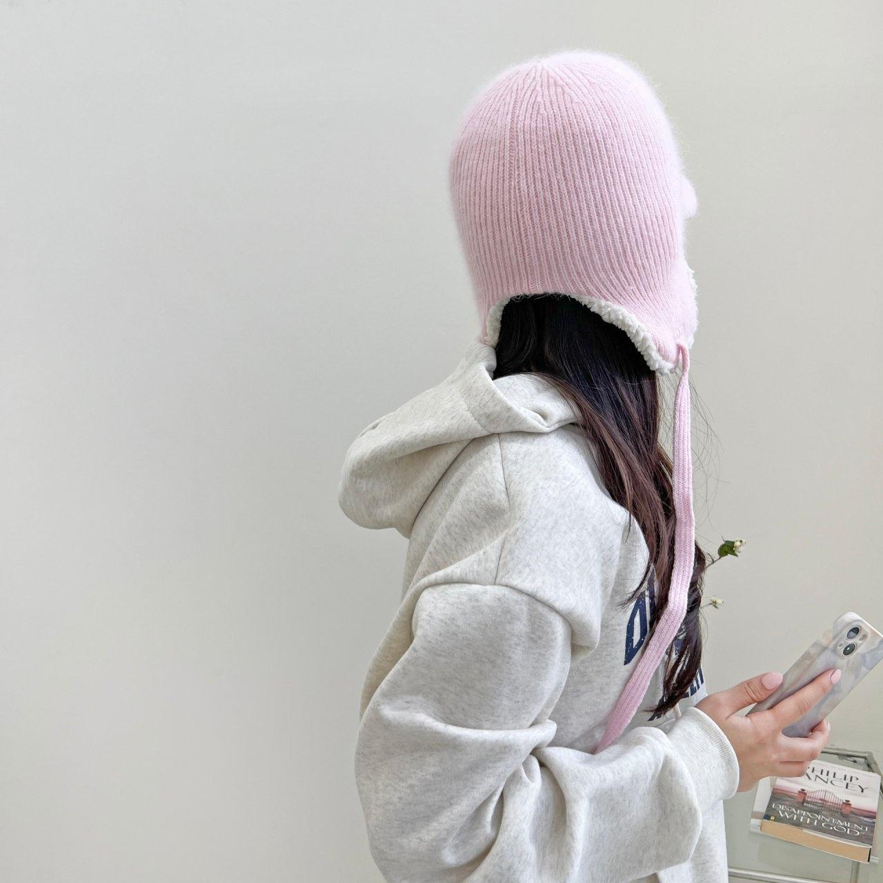 Person wearing a pink angora trapper - earflap hat with tie strings, paired with a gray hoodie