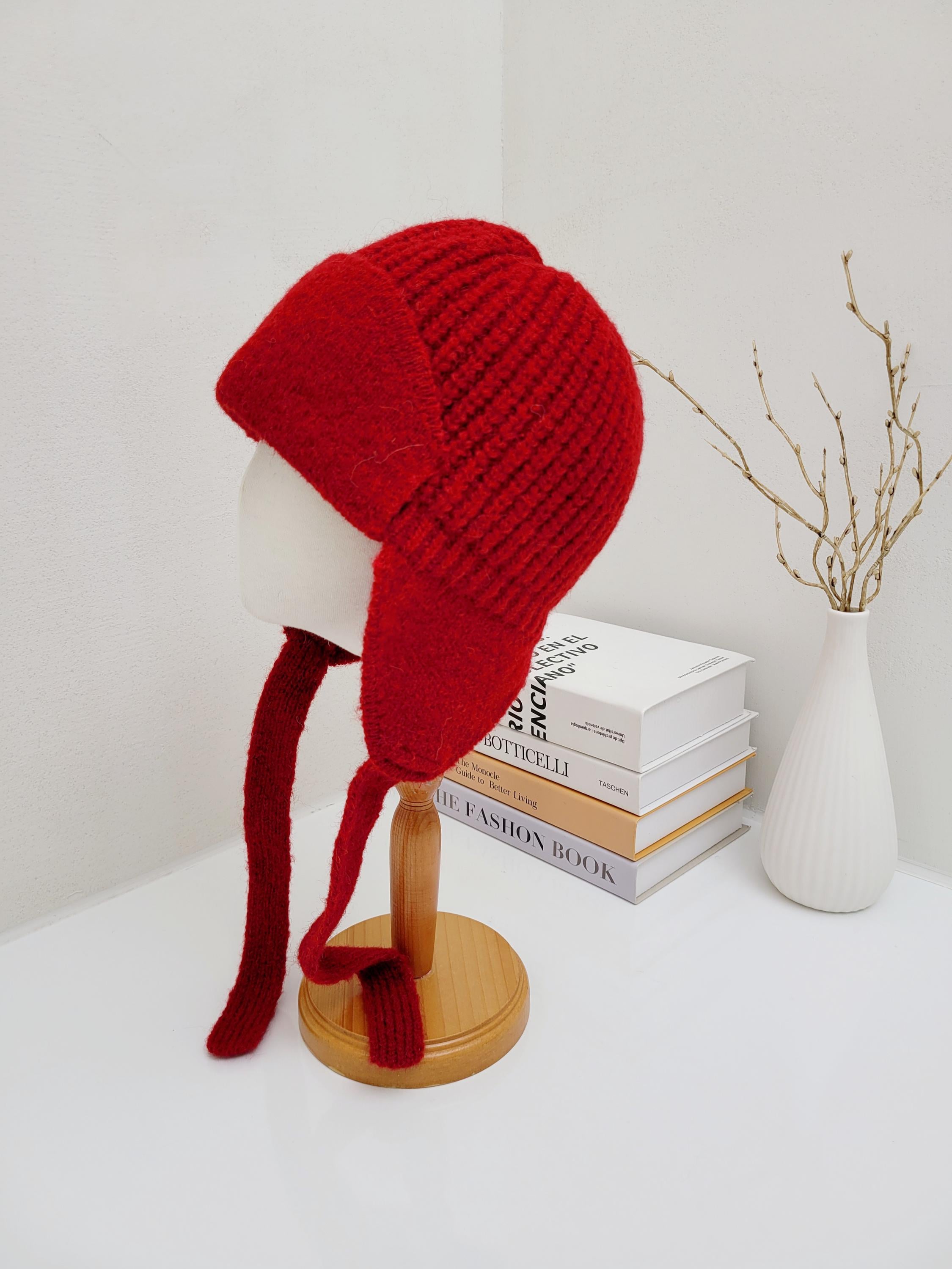 Red amelia knit hat with ear flaps, displayed on a mannequin head. Cozy and stylish winter headwear.