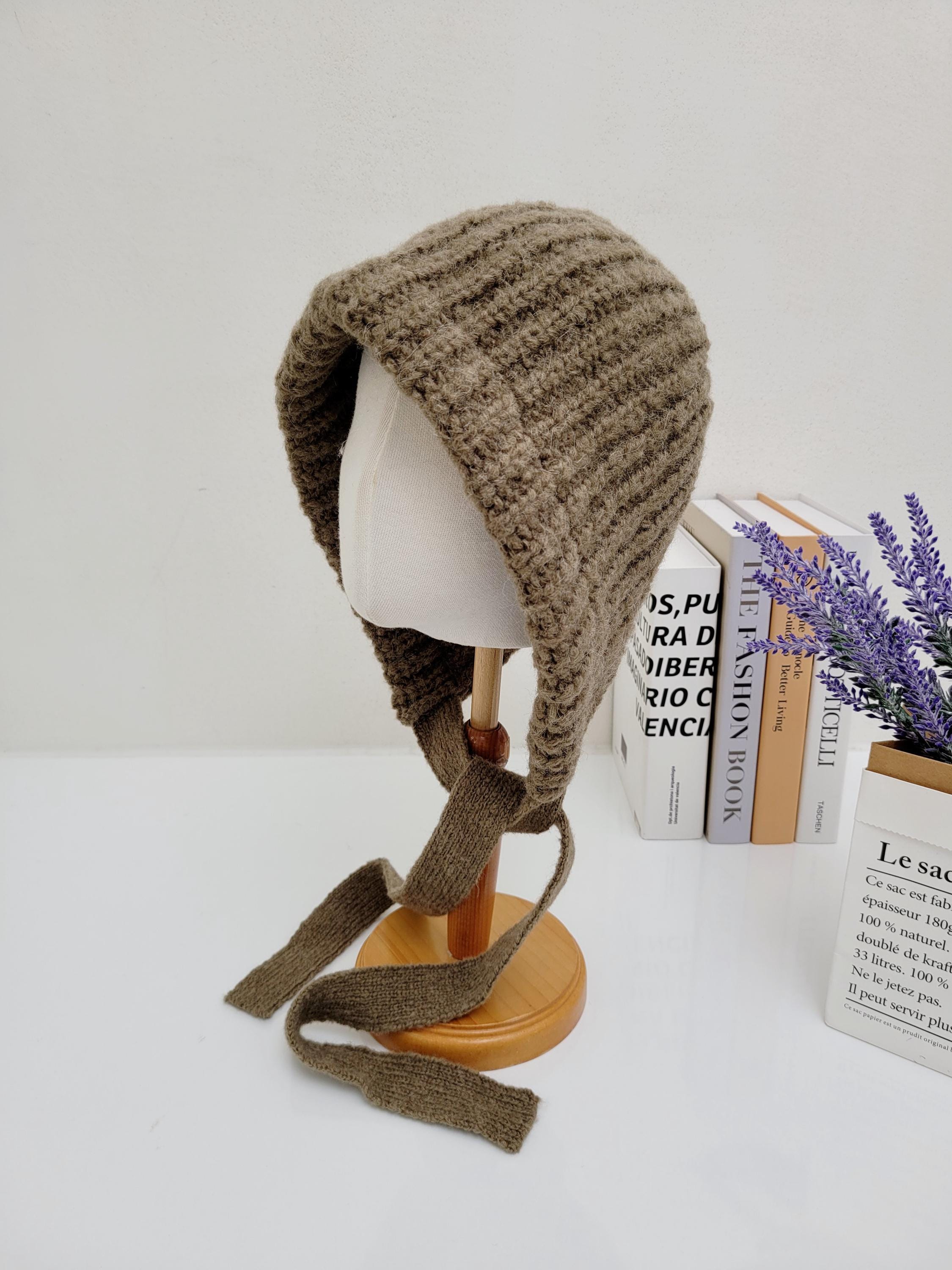 Brown knit tour le jour bonnet with attached ties, displayed on a mannequin head. A cozy, stylish head covering.