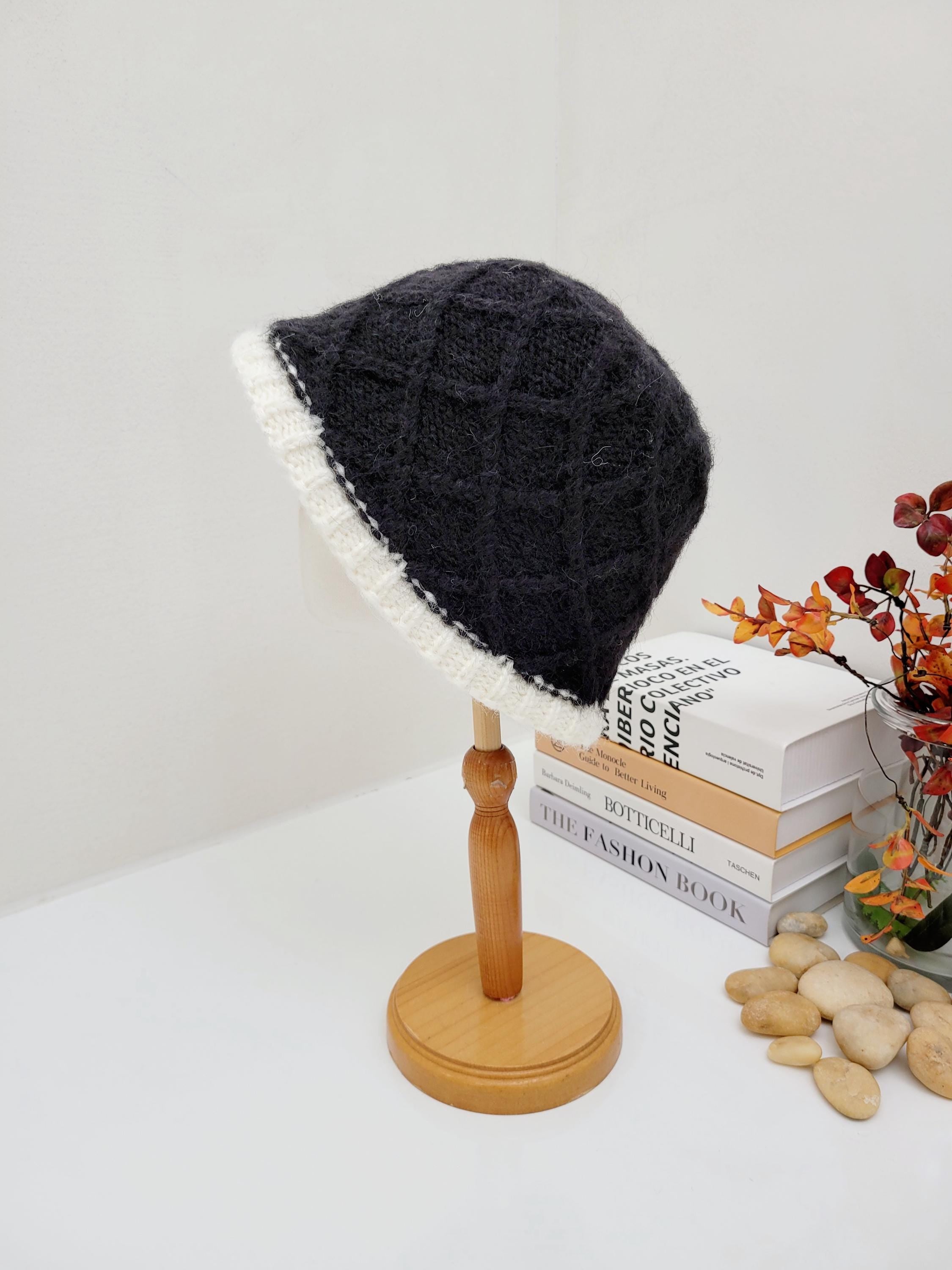 winter in the paris: a cozy, textured black knitted hat with a stylish white brim, displayed on a wooden stand.