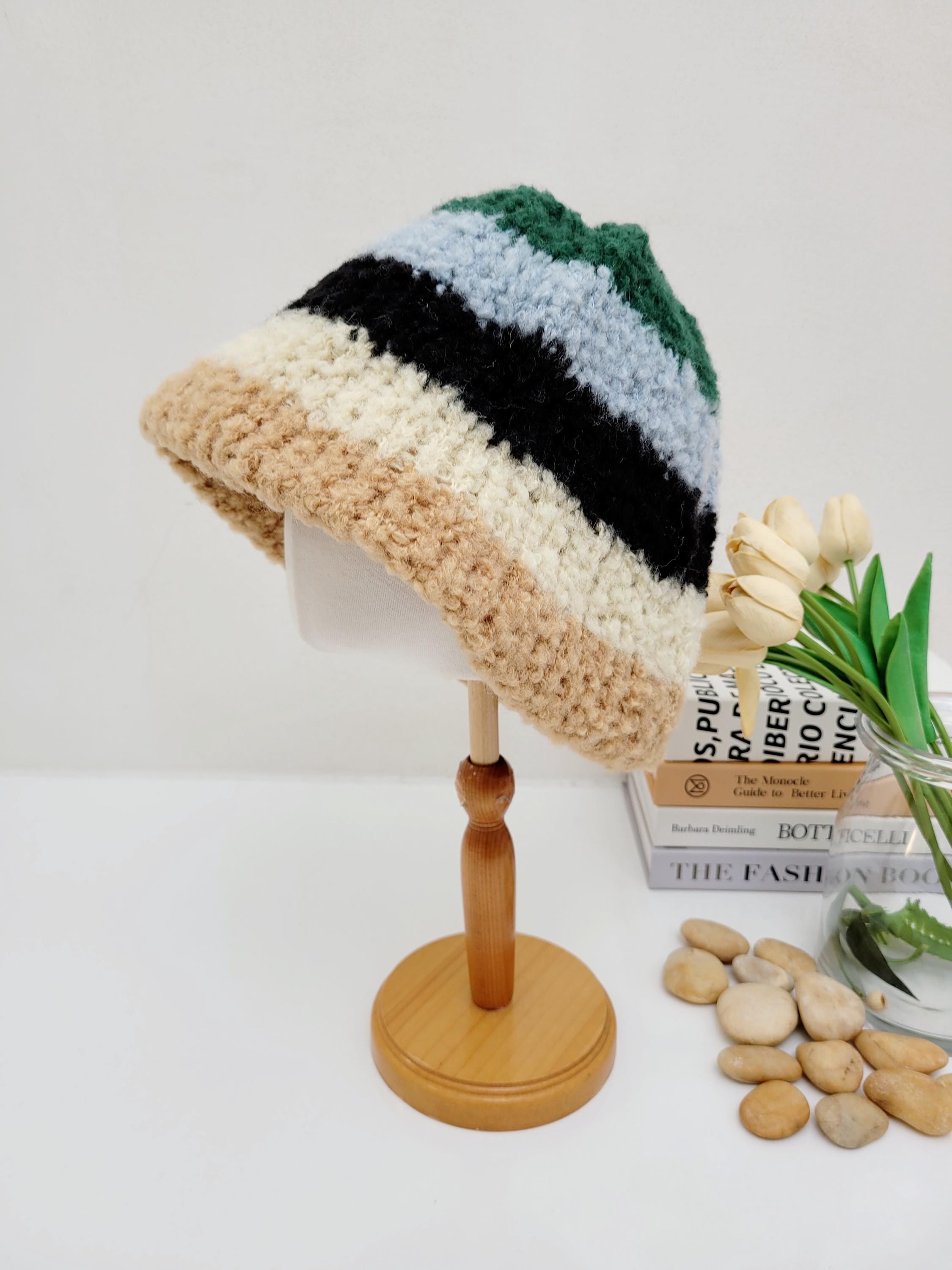 Striped tokyo beanie in beige, black, light blue, and green. A cozy, textured bucket hat on a wooden display stand.