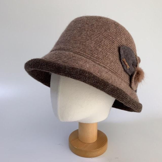 Brown knit hat, linda's favorite, with a dark brown brim, a fabric flower and a small pompom accent.