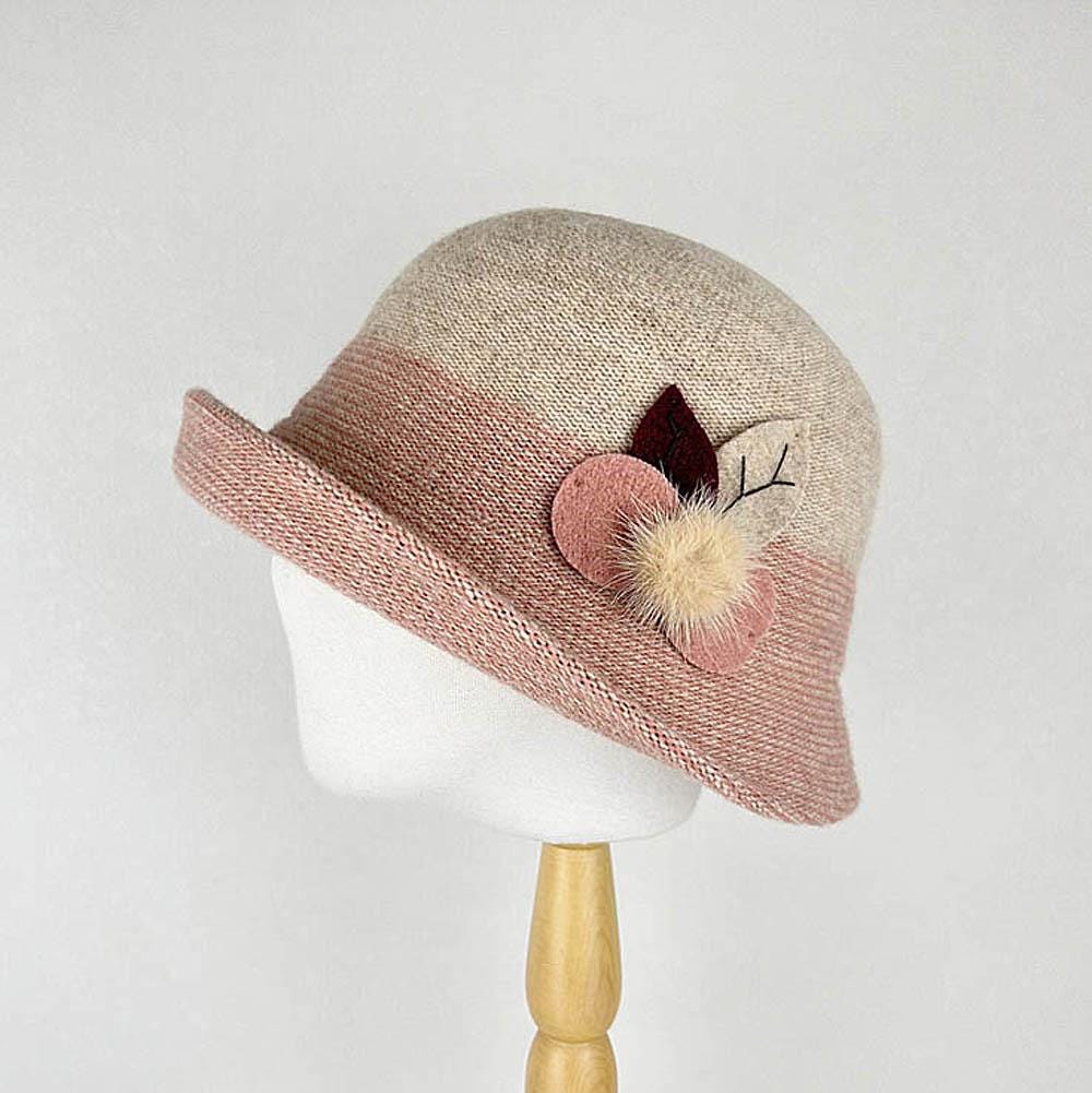 Beige and pink knit catherine cloche hat with floral details, including felt leaves and a pompom, displayed on a stand.