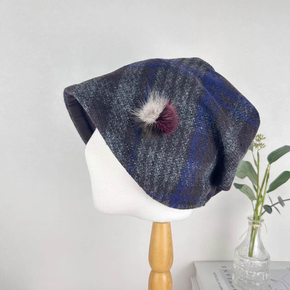 Checkered slouch hat in blue, gray, and brown with a decorative pompom, displayed on a mannequin head.