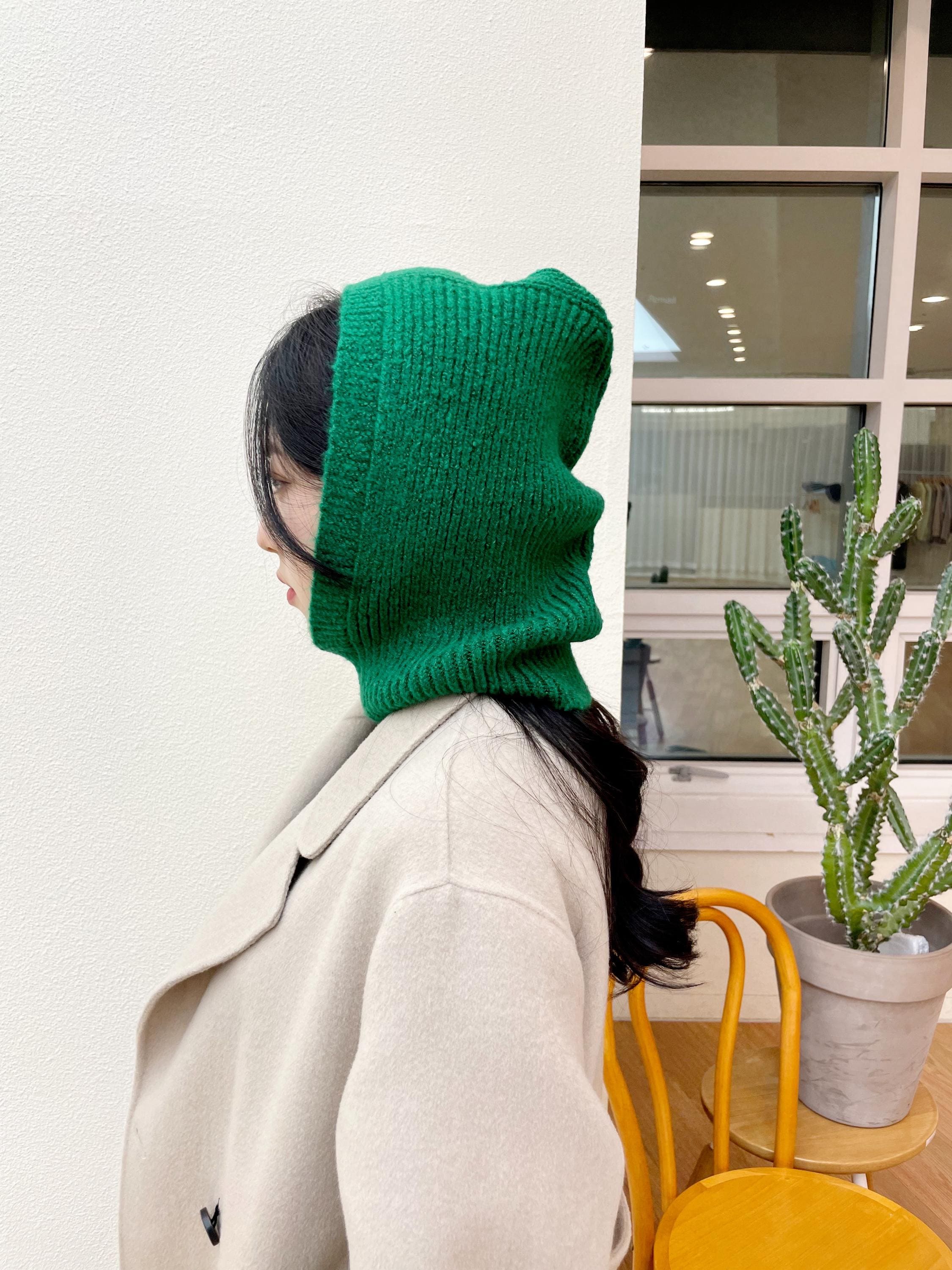 LITTLE RIDING HOOD Balaclava: Woman in green knitted balaclava and beige coat.