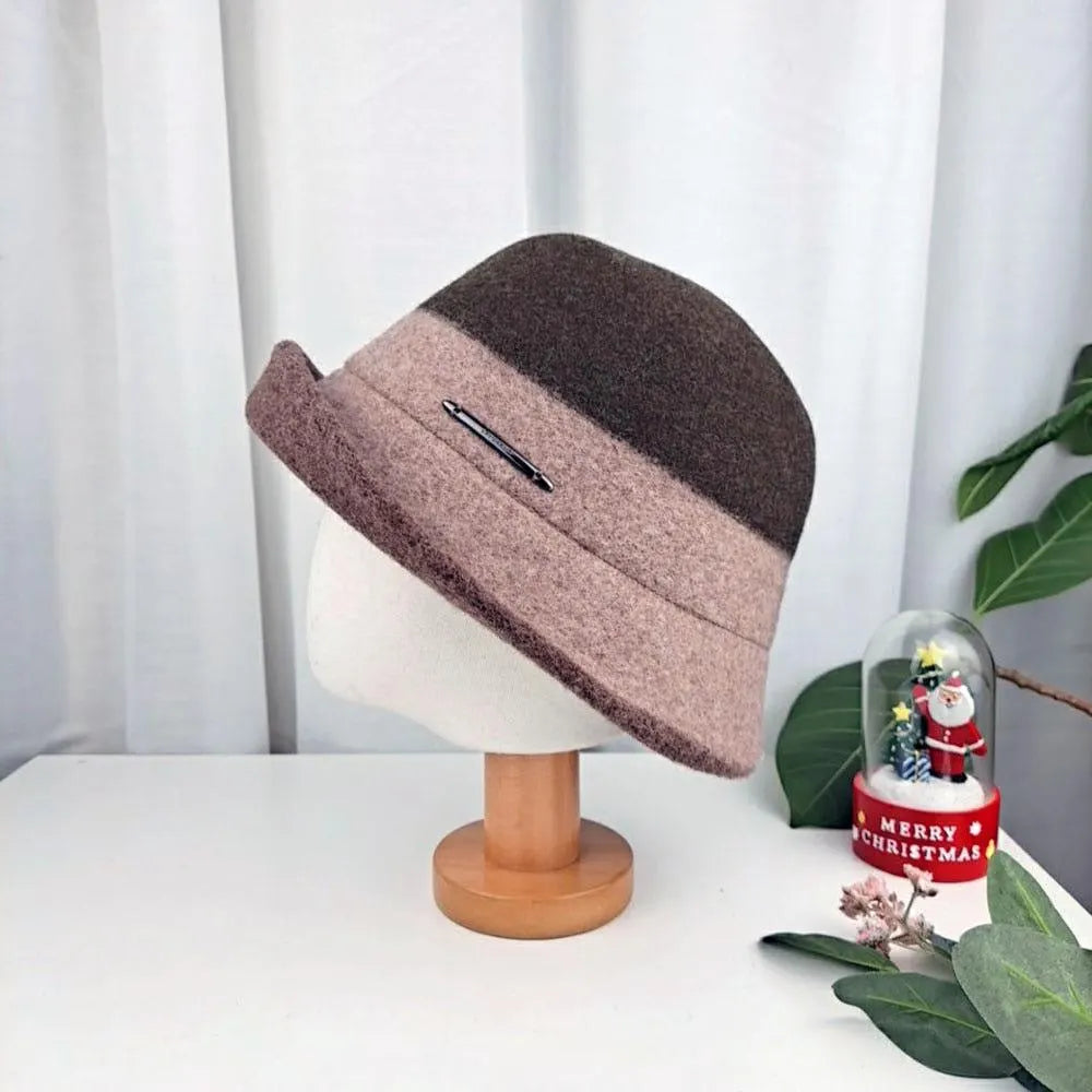 3tone wool bucket hat in brown and mauve, displayed on a wooden stand with a subtle metal accent.