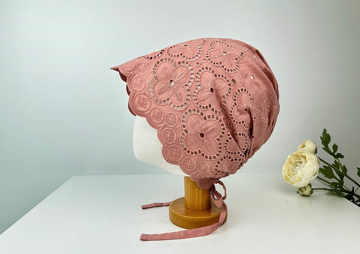 Dusty rose eyelet beanie with delicate floral lace trim, shown on a mannequin head. The eyelet beanie has a tie closure.