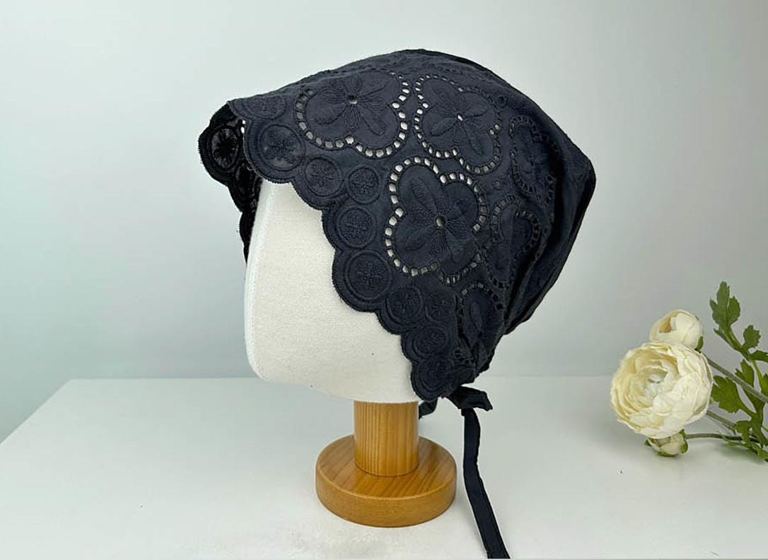 Black EYELET BEANIE featuring intricate floral eyelet lace trim and a tie closure, displayed on a mannequin head.